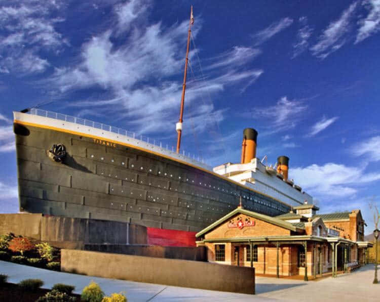 Museum 桌布 壁紙 — 一艘巨大的鐵達尼號複製品停靠在歷史悠久的磚造車站旁，天空湛藍，雲朵輕柔。