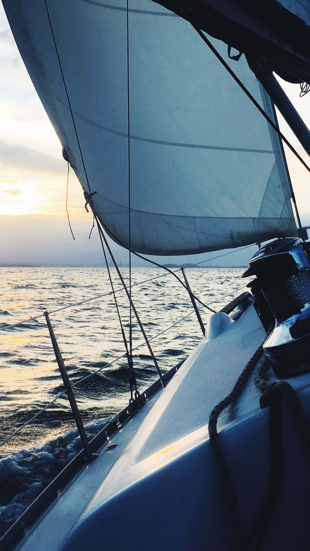 Sailboat 桌布 壁紙 — 一艘帆船在日落時分滑過平靜的水面，金色的光芒反射在波浪和帆上。