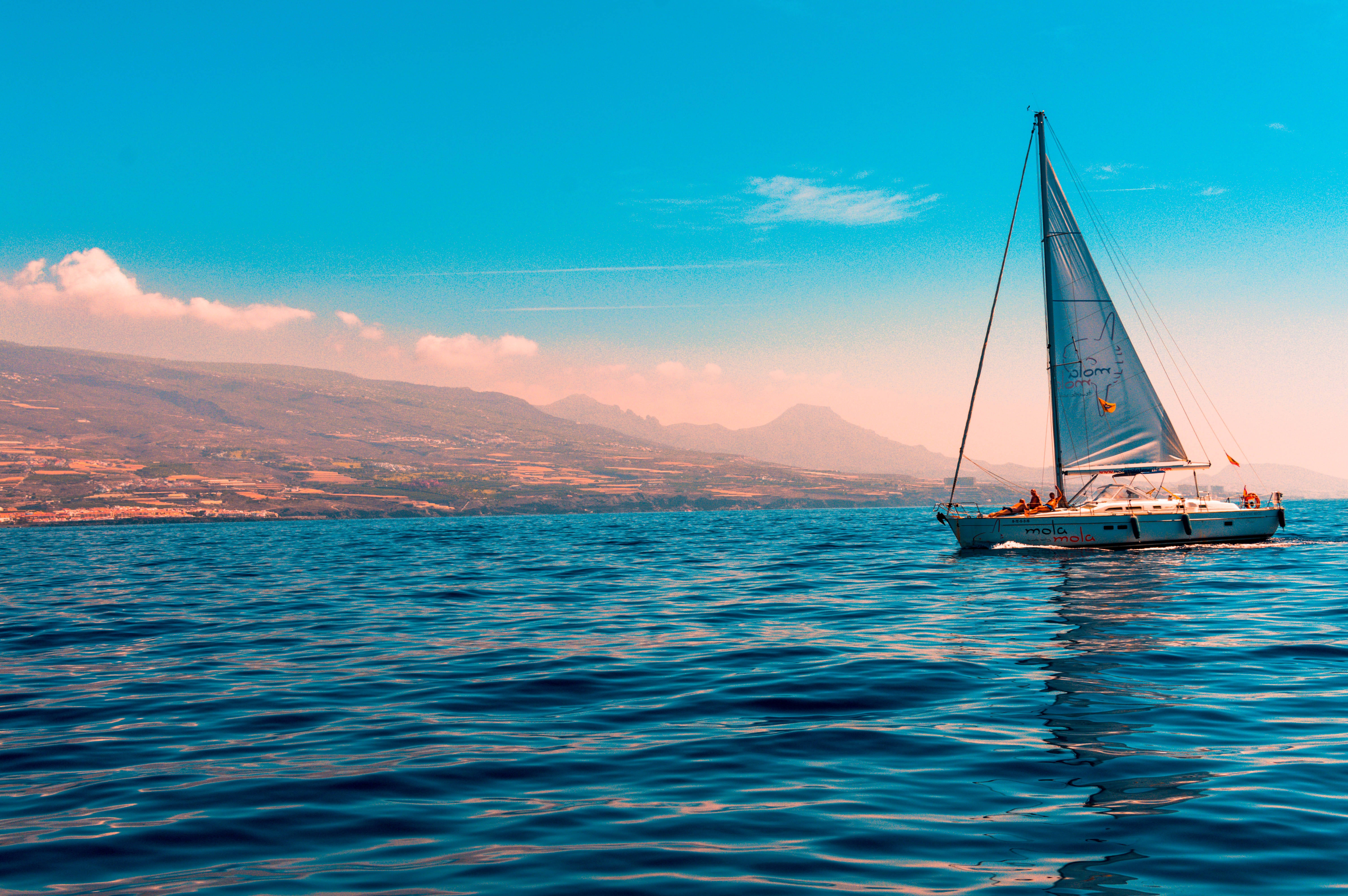 Yacht 桌布 壁紙 — 一艘帆船在深藍色的水面上滑行，遠山在充滿活力的青綠色天空下。