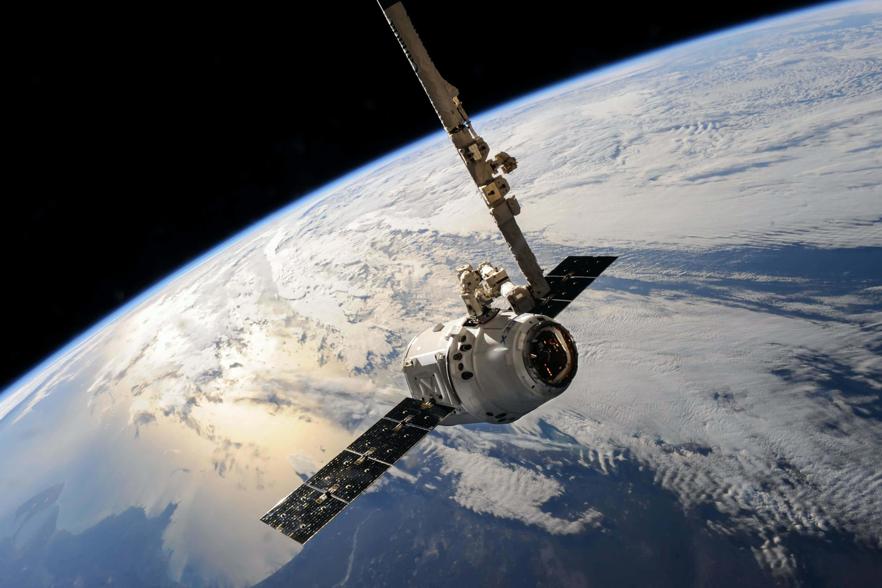Space Satellite 桌布 壁紙 — 一艘帶有太陽能板的太空船繞地球軌道運行，顯示被雪覆蓋的大陸和海洋，背景是太空的漆黑。