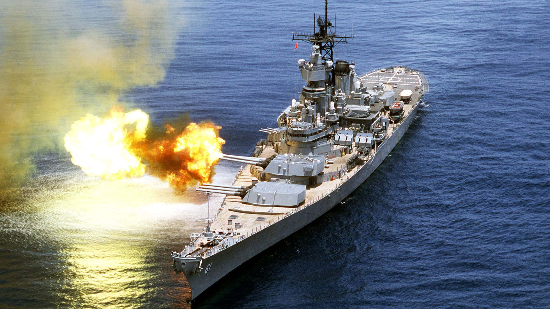 Navy 桌布 壁紙 — 一艘戰艦在開闊的海洋上發射巨型火炮，爆炸性的火焰和濃煙在深藍色海水中翻騰。