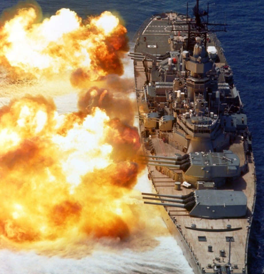 Battleship 桌布 壁紙 — 一艘戰艦發射巨型火炮，在晴朗的藍天下向海洋中噴射出熾熱的橙色爆炸。