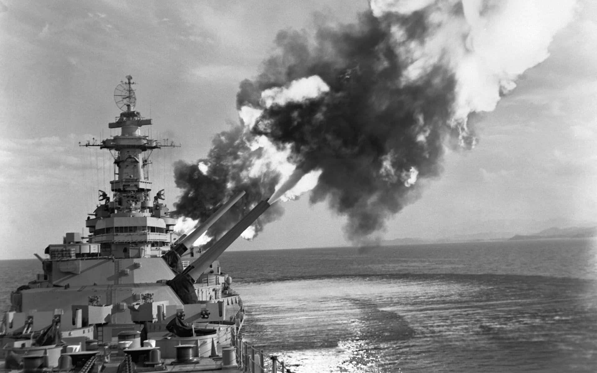 Battleship 桌布 壁紙 — 一艘戰艦發射巨型火炮，濃煙和火焰沖向海洋上方的天空。