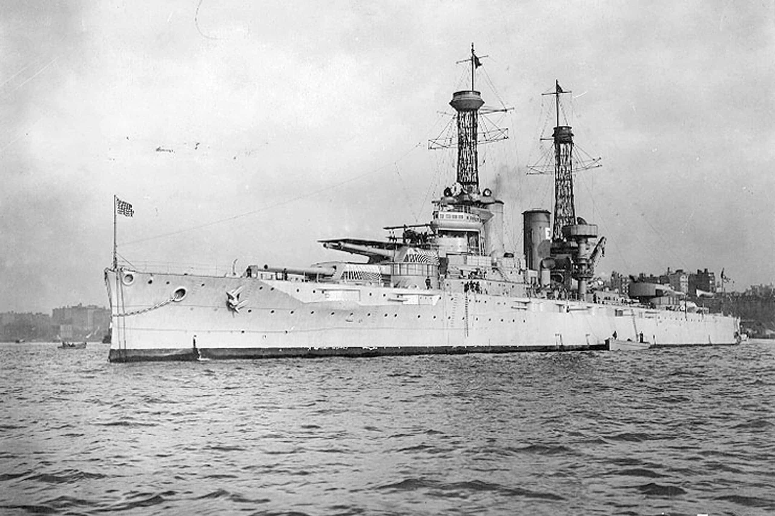 Battleships 桌布 壁紙 — 一艘擁有高聳砲塔和煙囪的巨大戰艦，在陰天之下平靜地漂浮在漣漪的水面上。