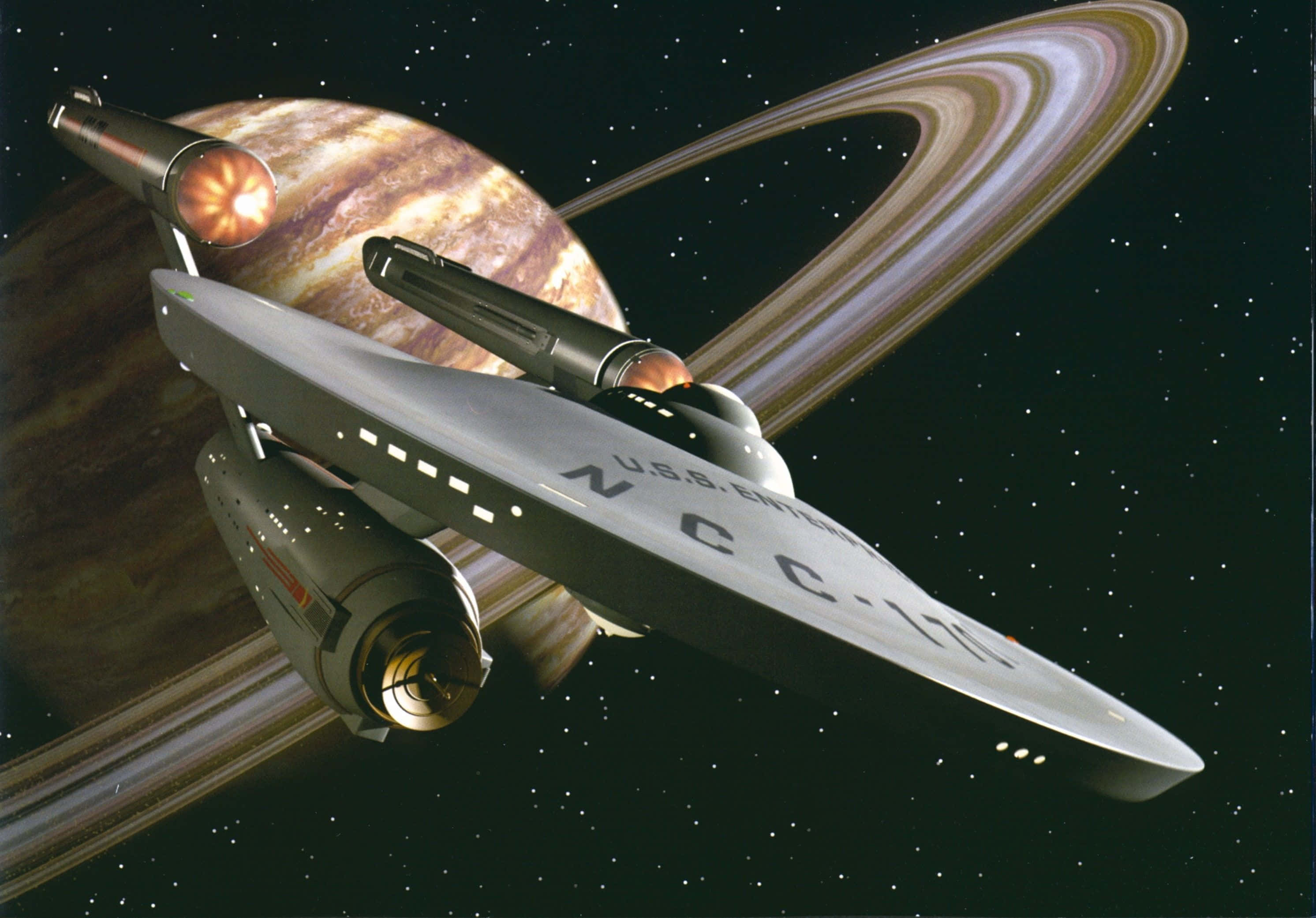 Star Trek Enterprise 桌布 壁紙 — 一艘星際飛船在星光璀璨的太空背景下，飛過一顆帶有光環的行星，引擎發出光芒。