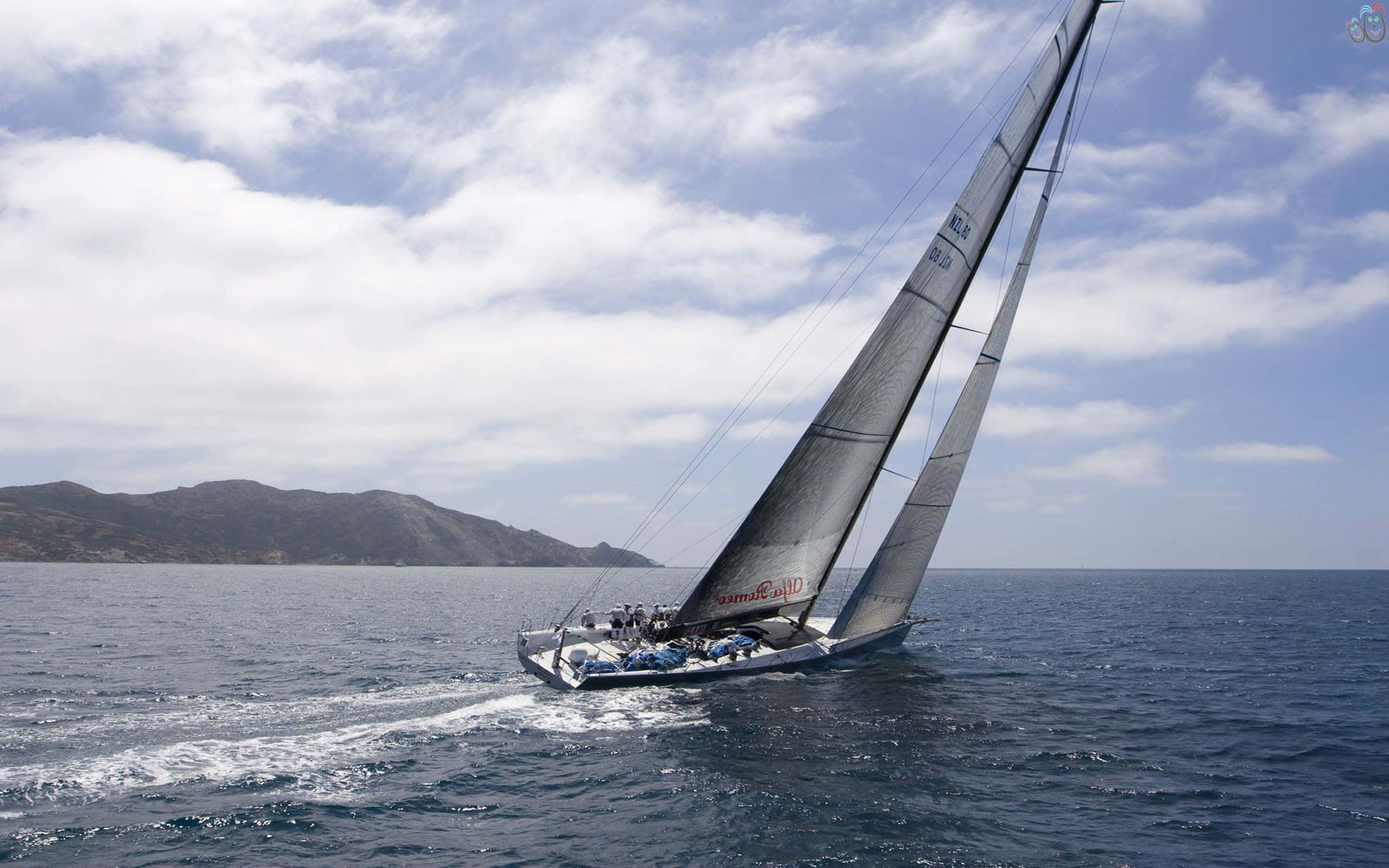 Sailboat 桌布 壁紙 — 一艘時尚帆船，高聳的帆在深藍色海水中劃過，留下白色尾跡，天空部分多雲，遠方有山丘。