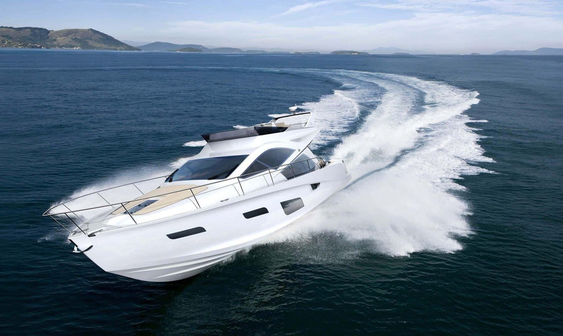 Yacht 桌布 壁紙 — 一艘時尚的白色機動遊艇劃過深藍色海水，在明亮的天空下，在遠處丘陵海岸線的映襯下留下泡沫般的尾跡。