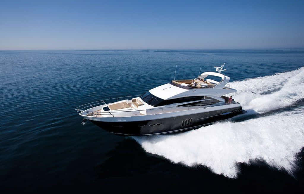 Yacht 桌布 壁紙 — 一艘時尚豪華遊艇在深藍色海洋中破浪前行，在晴朗天空下留下白色泡沫尾跡。