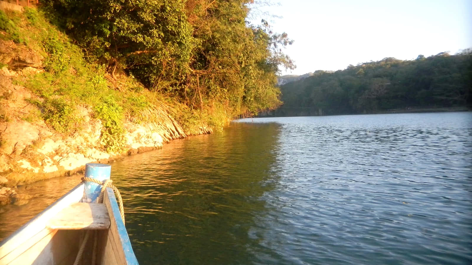 river 桌布 壁紙 — 一艘木船在平靜的河流上滑行，兩岸綠樹成蔭，溫暖的金色陽光灑落。