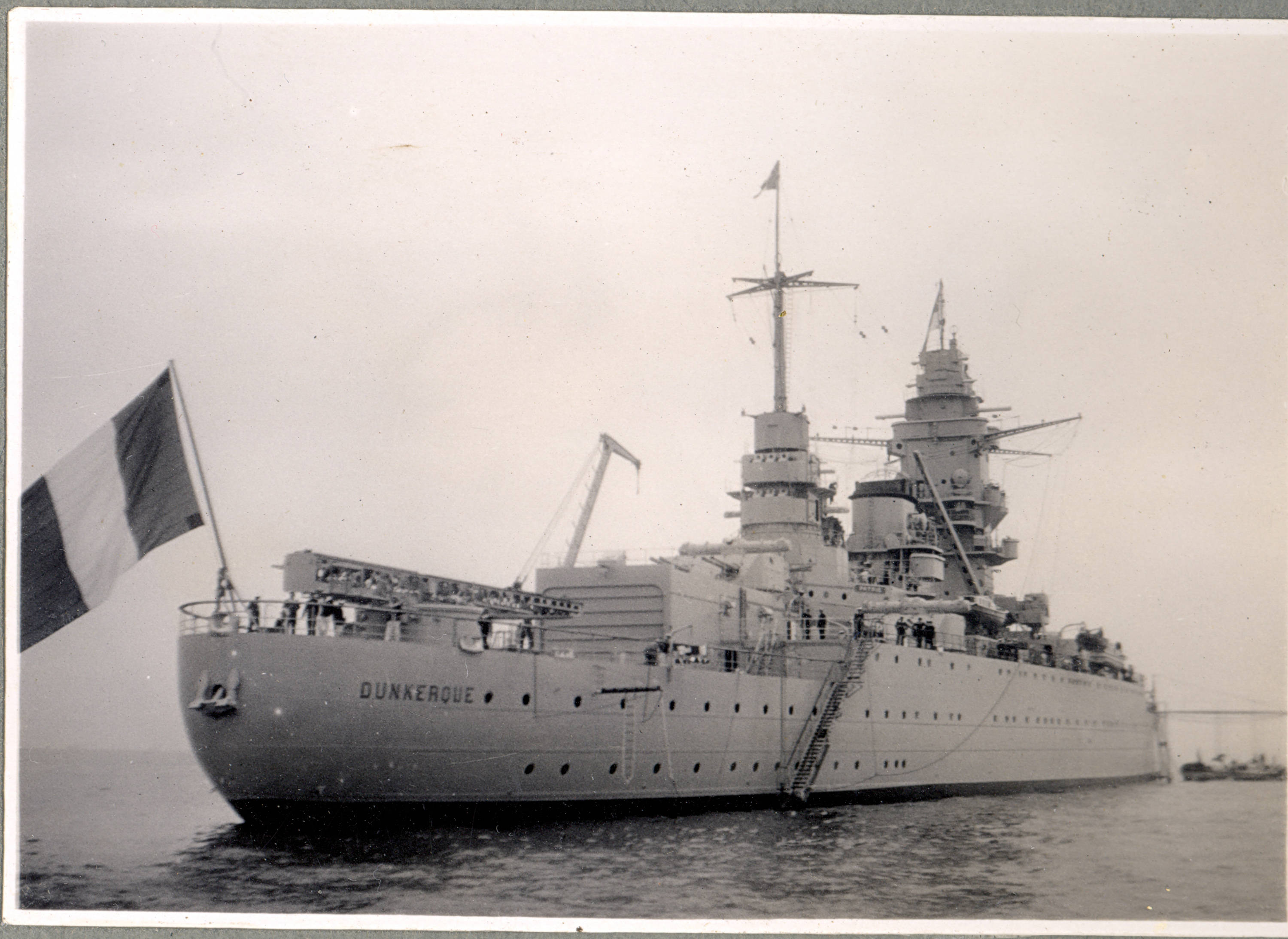 french 桌布 壁紙 — 一艘歷史悠久的法國戰艦敦克爾克在平靜的水面上漂浮，旗幟飄揚，甲板上可見船員。
