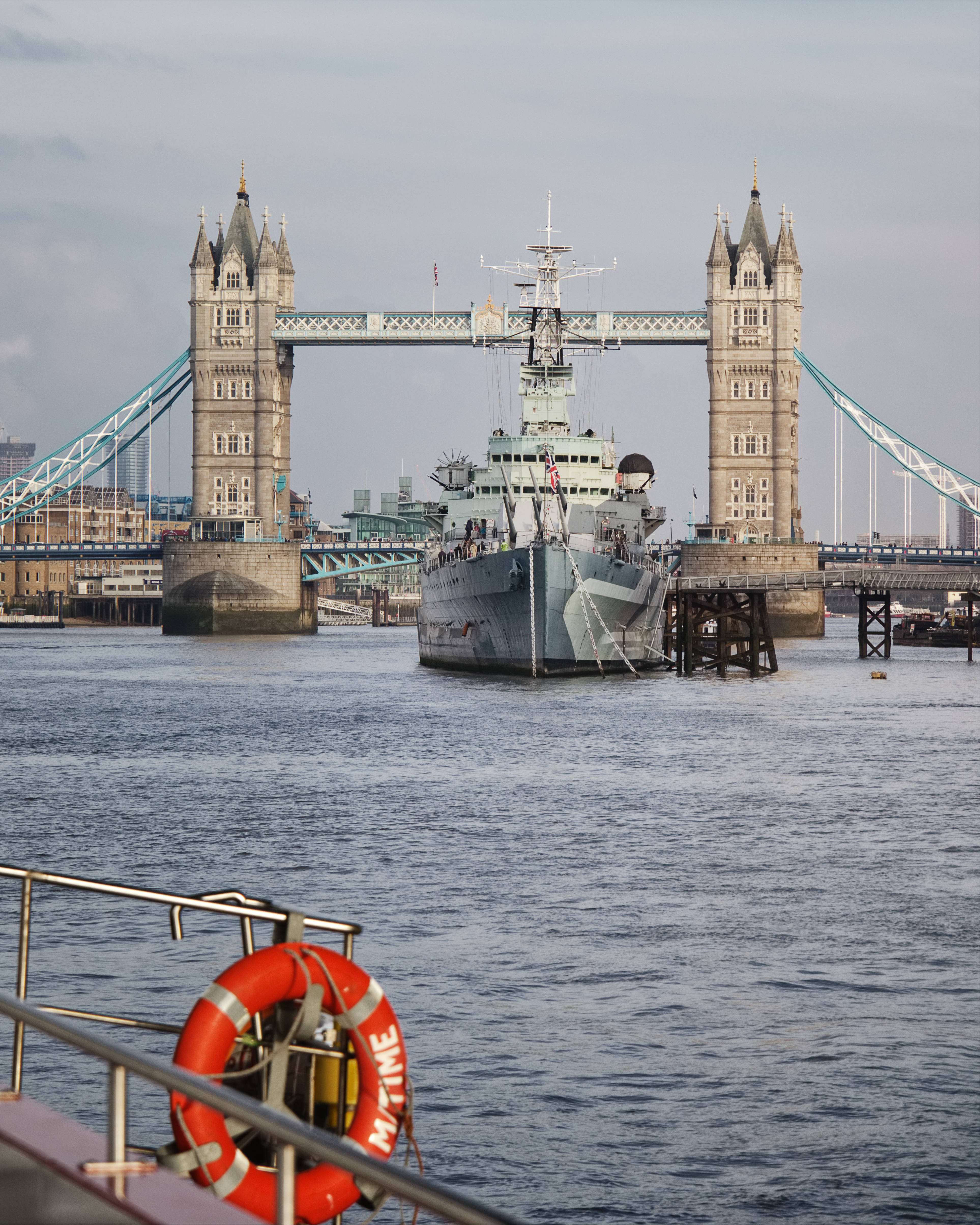 Warship 桌布 壁紙 — 一艘歷史戰艦停泊在泰晤士河上，倫敦塔橋在陰天背景下高聳入雲。