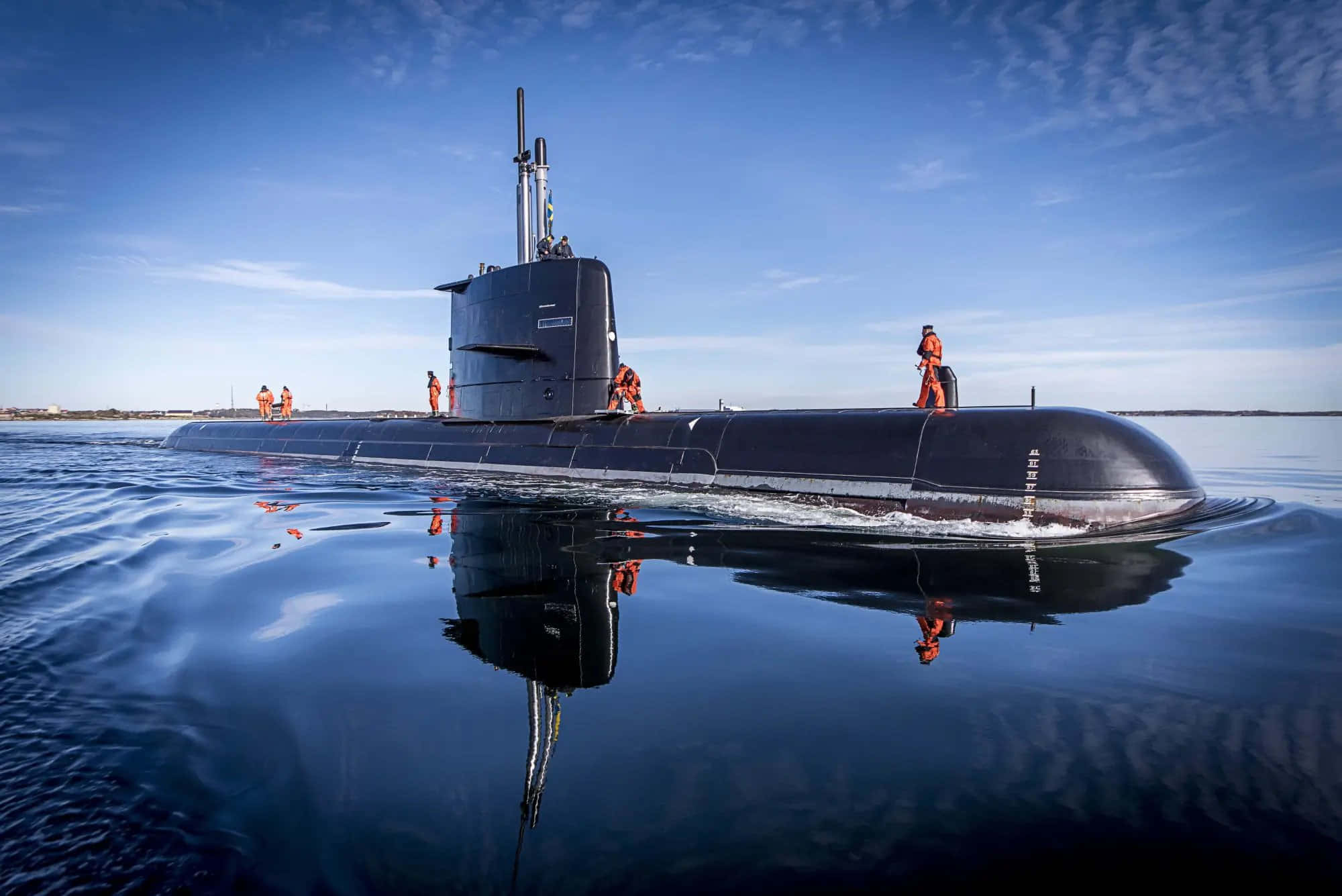 Submarine 桌布 壁紙 — 一艘流線型黑色潛艇在平靜的藍色水面上浮出，穿著橙色裝備的船員站在甲板上，天空晴朗。