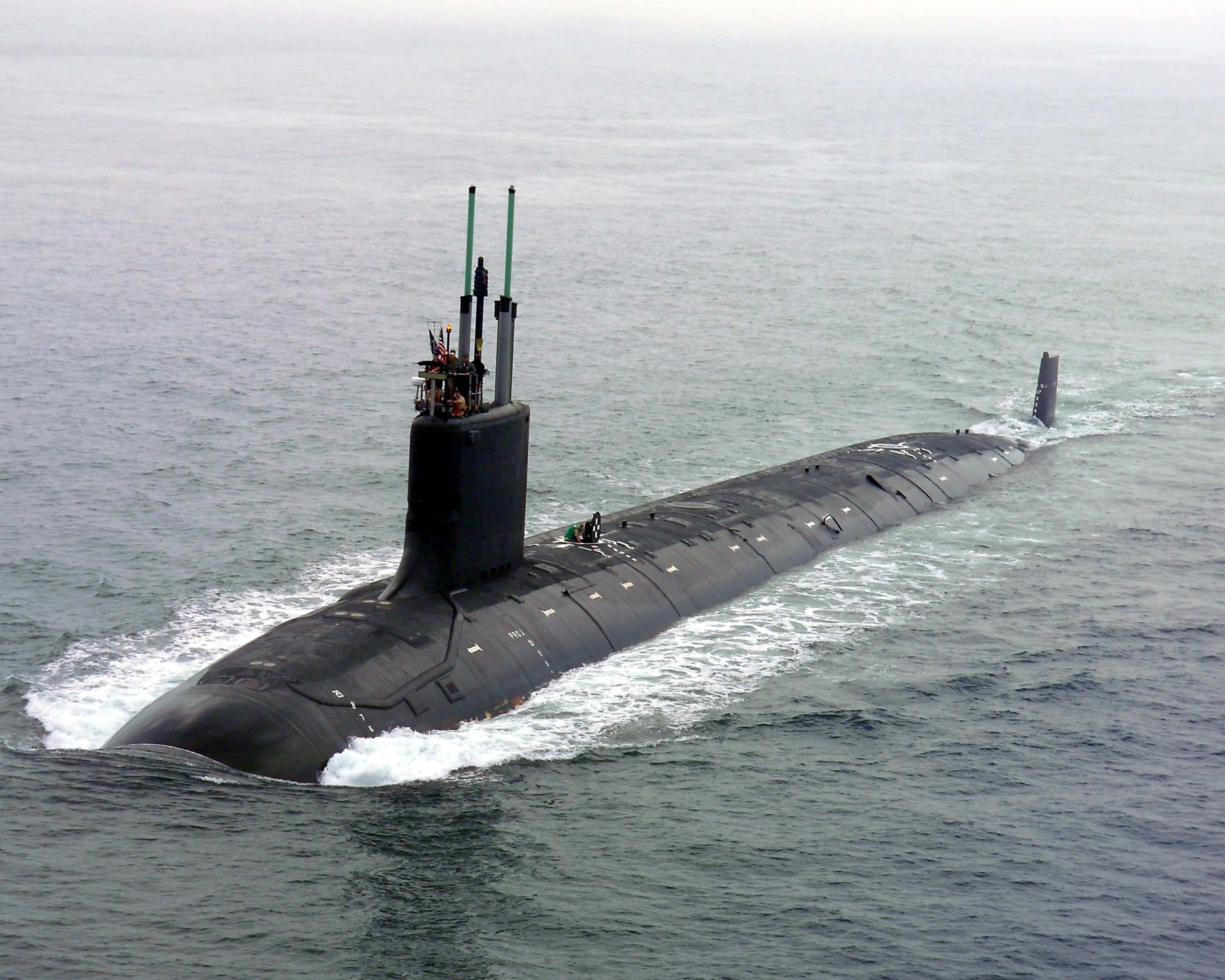 Submarine 桌布 壁紙 — 一艘流線型黑色潛艇穿過波濤洶湧的灰色海水浮出水面，留下白色尾跡。