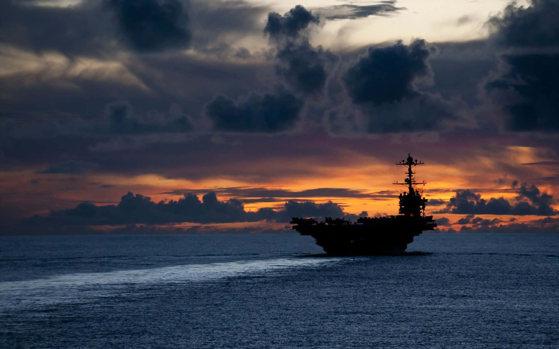 Navy 桌布 壁紙 — 一艘海軍航空母艦在開闊的海洋水域上，以戲劇性的日落天空為背景呈現剪影。