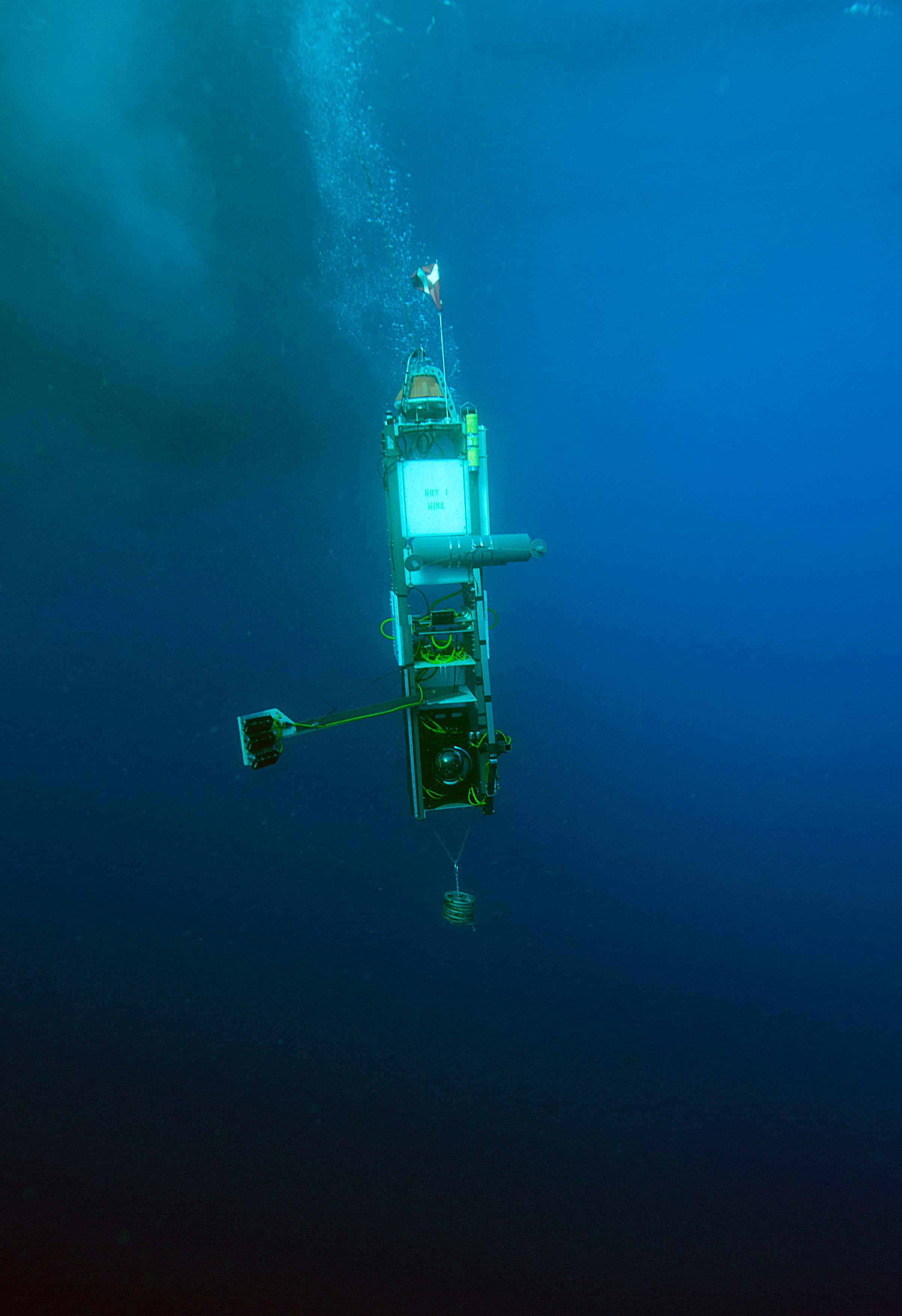 Mariana Trench 桌布 壁紙 — 一艘深海潛水器在廣闊的深藍色海洋中發出人造光，下降時拖曳著氣泡。