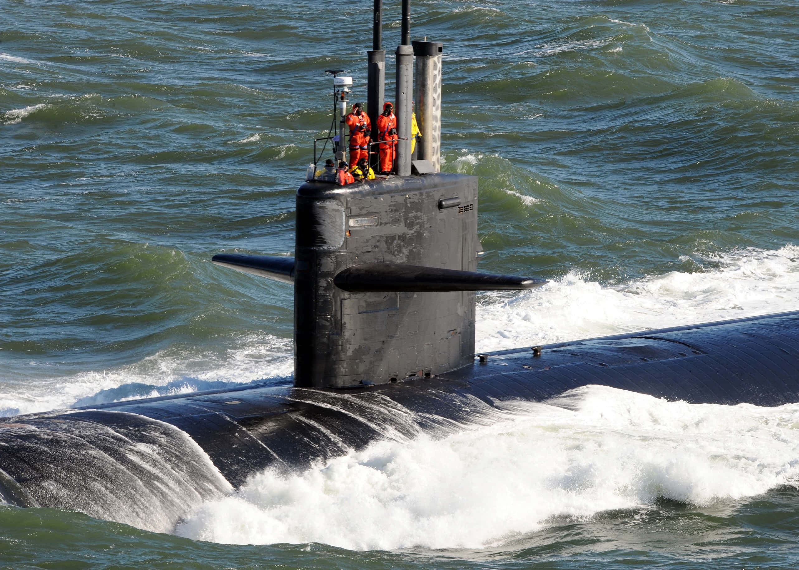Submarine 桌布 壁紙 — 一艘深色潛艇穿過波濤洶湧的綠色海水浮出水面，指揮塔上有穿著橙色服裝的船員。