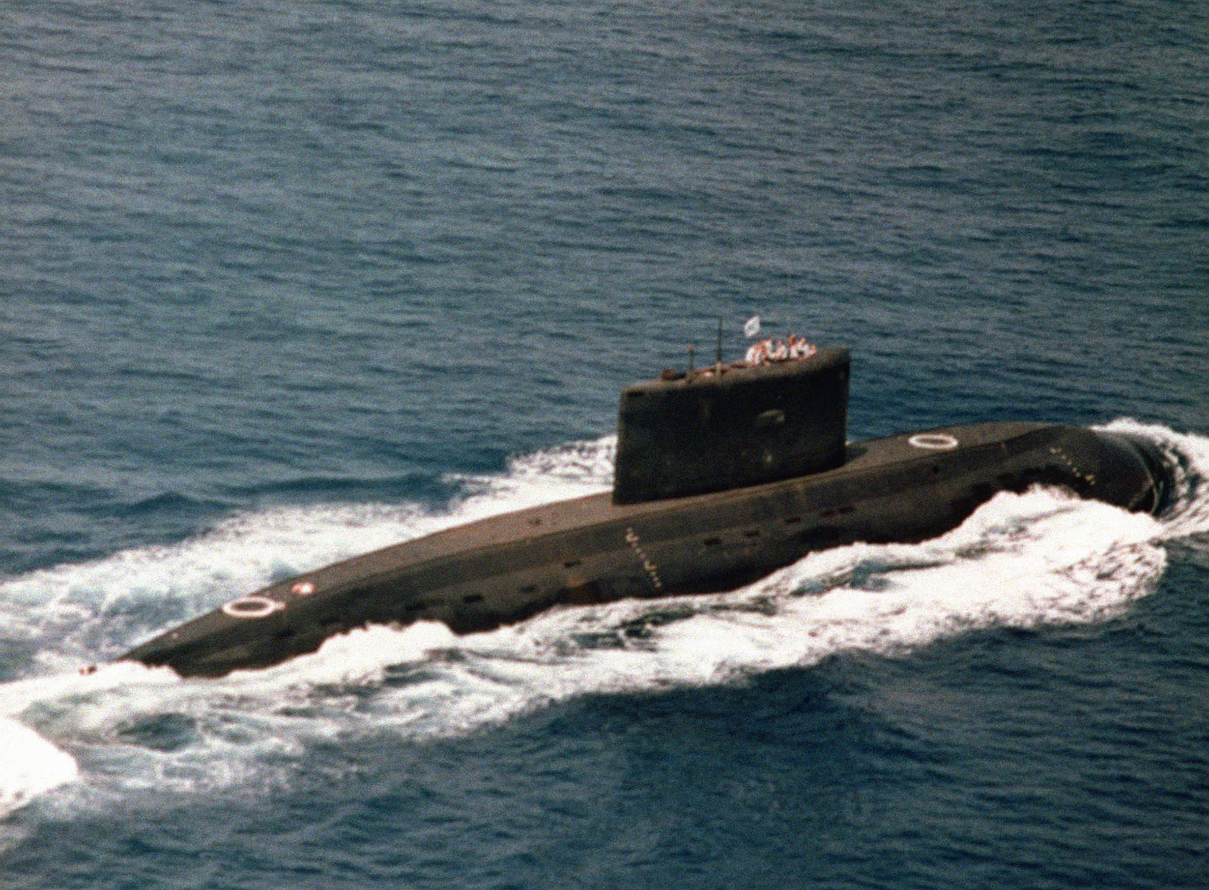 Submarine 桌布 壁紙 — 一艘深色潛艇穿過波濤洶湧的藍色海水浮出水面，在其流線型船體後留下白色泡沫痕跡。