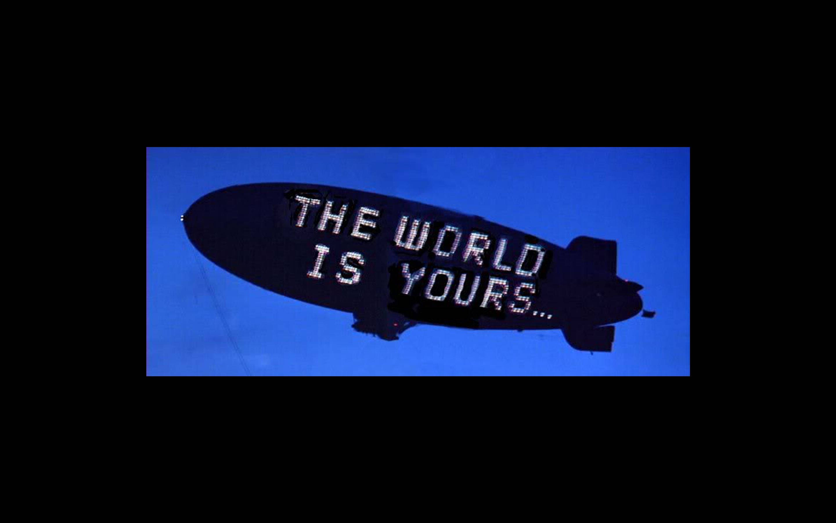 fly 桌布 壁紙 — 一艘深色飛船帶有發光的像素文字寫著「THE WORLD IS YOURS...」，漂浮在深藍色的夜空背景下。