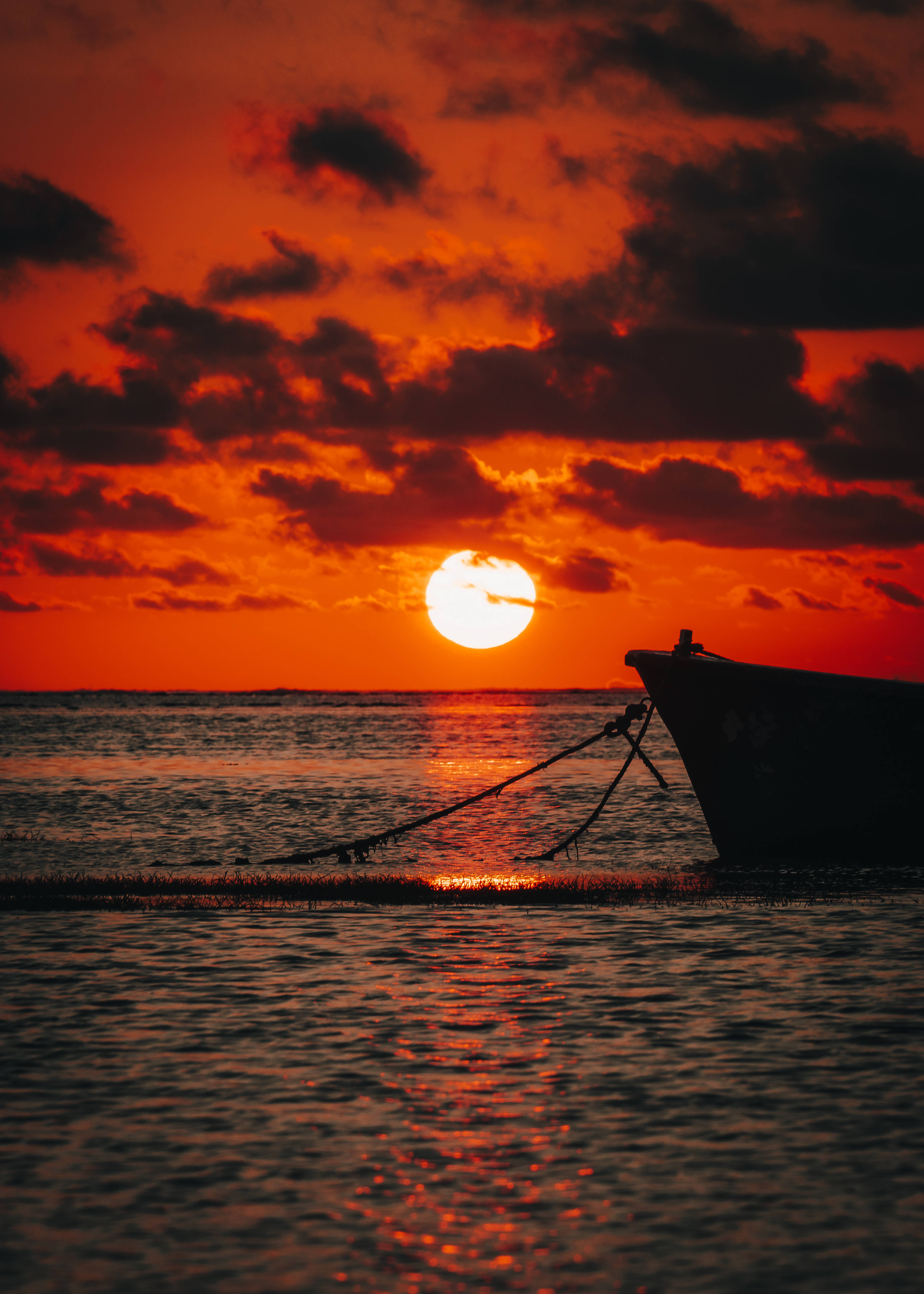 Mauritius 桌布 壁紙 — 一艘漁船的剪影在發光的橙色水面上，太陽在戲劇性的雲層後落下。