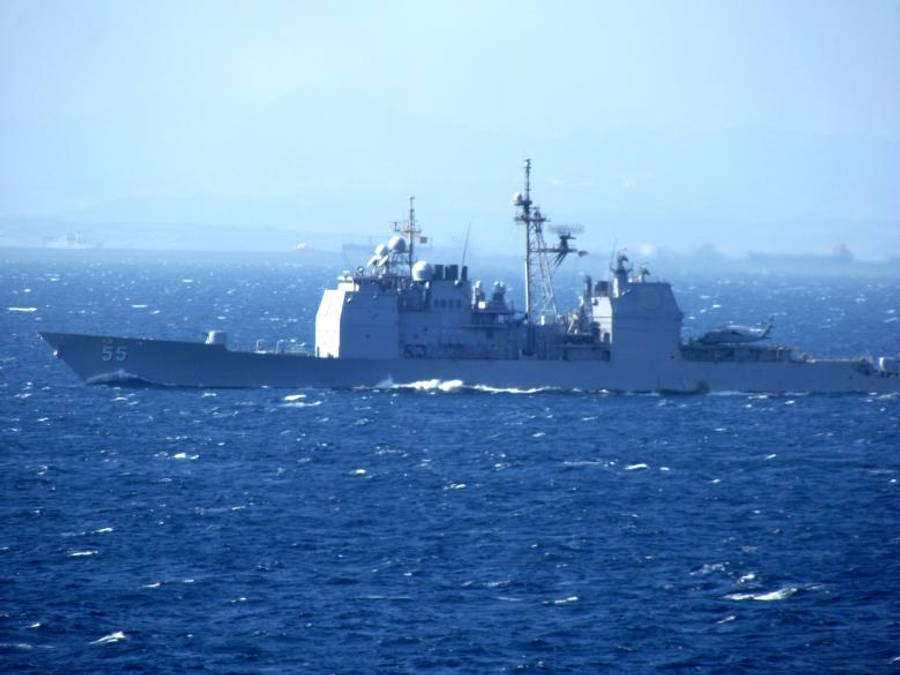 u s navy 桌布 壁紙 — 一艘灰色海軍驅逐艦在朦朧的天空下劃過深藍色的海洋波浪，遠處可見陸地。