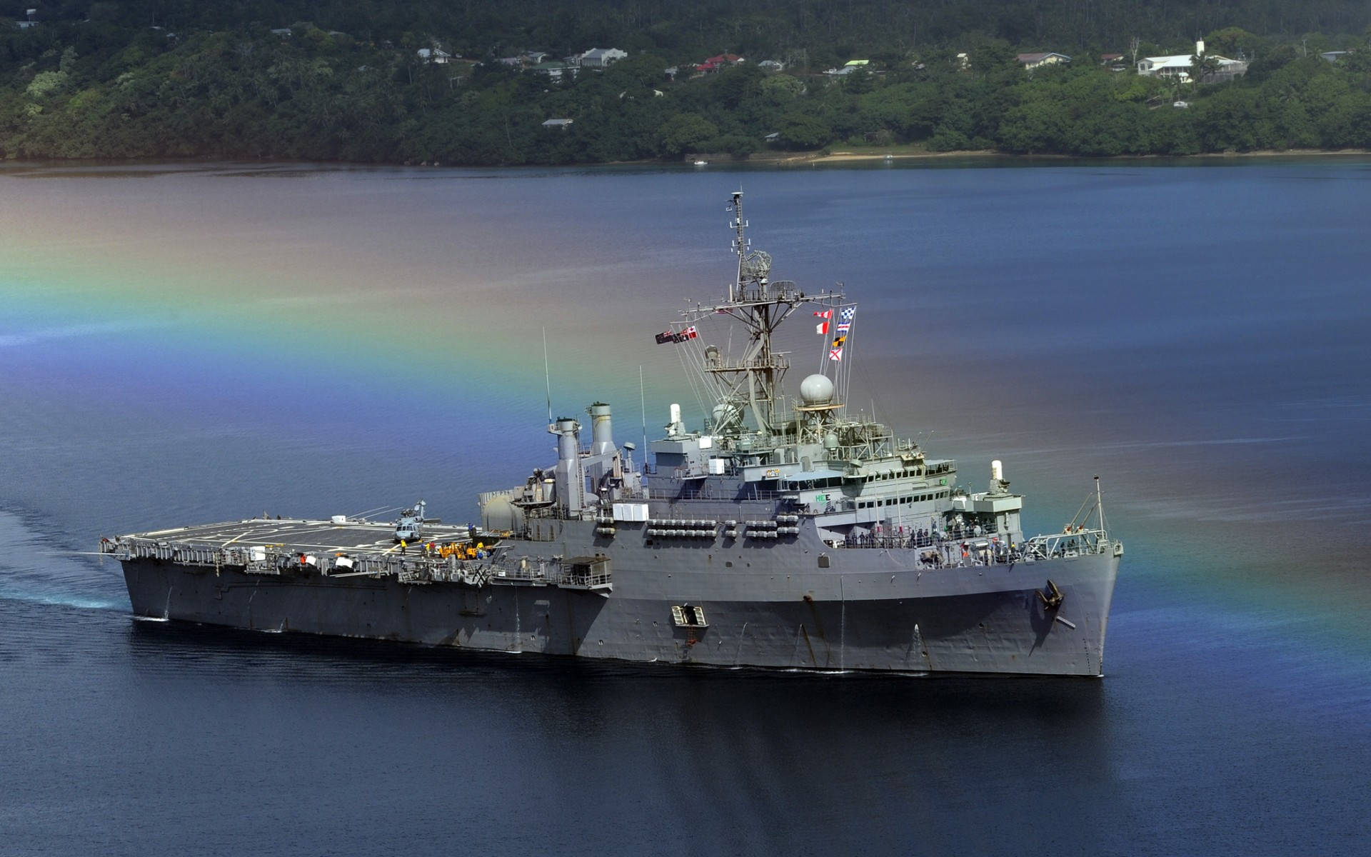 灰色軍艦在綠色海岸附近以彩虹為背景航行。