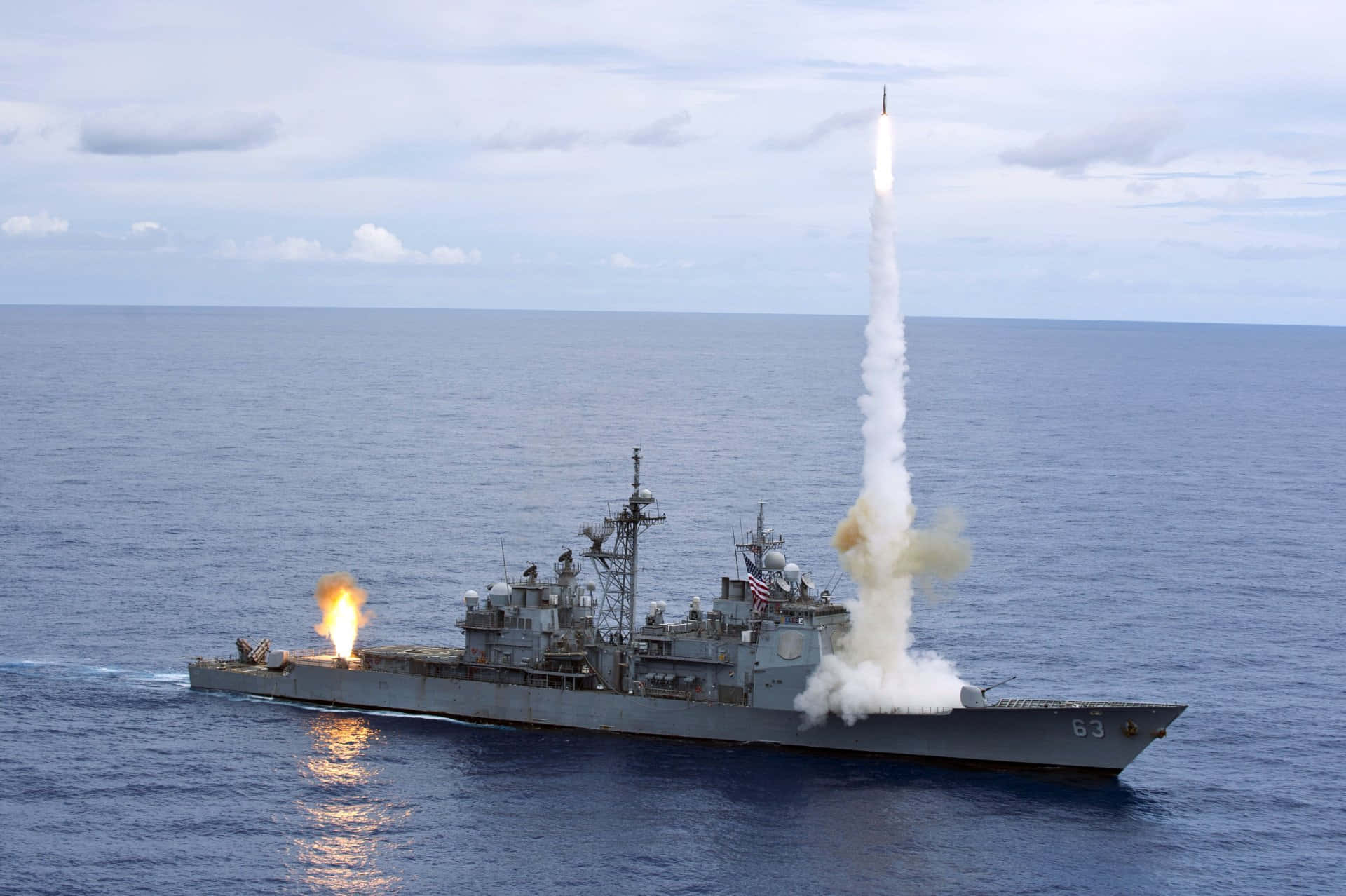 Navy 桌布 壁紙 — 一艘灰色軍艦在海洋上空發射飛彈，明亮的火焰和煙霧在陰雲密佈的天空中拖曳。