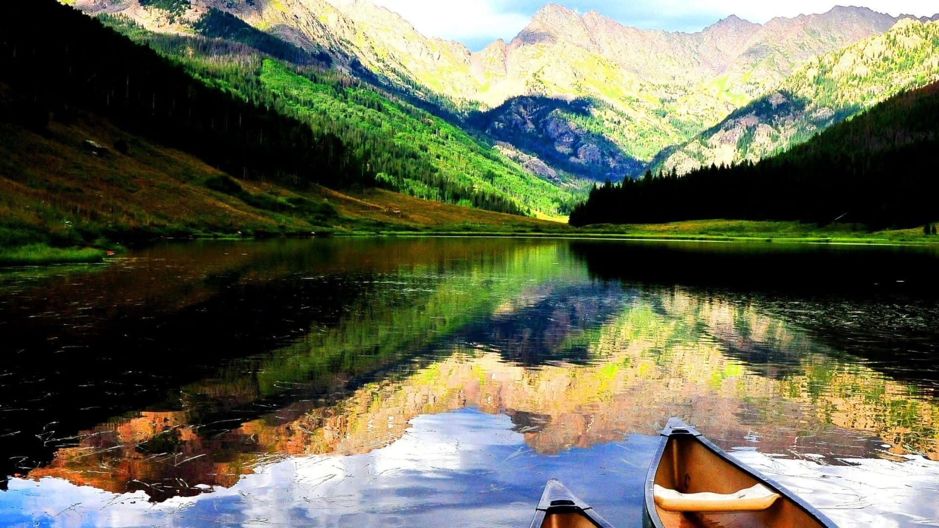 Colorado Mountains 桌布 壁紙 — 一艘獨木舟停泊在如鏡的山湖邊，倒映著翠綠的森林和陽光普照的山峰，天空湛藍清澈。