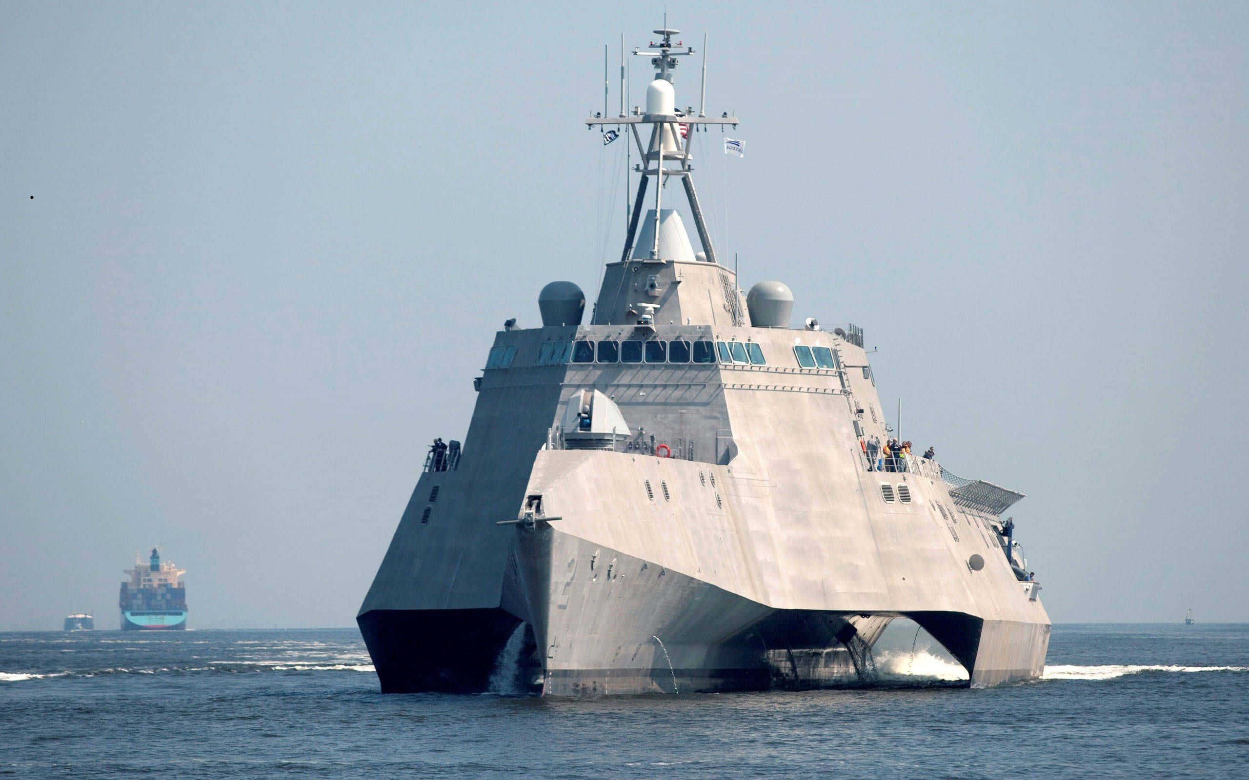 Navy 桌布 壁紙 — 一艘現代灰色軍艦以棱角設計劃破平靜的藍色海水，在朦朧的天空下留下白色航跡。