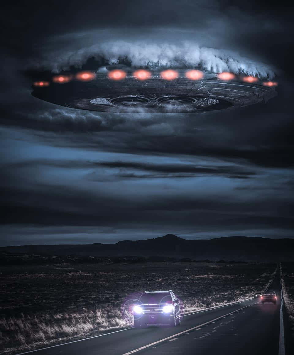 Road 桌布 壁紙 — 一艘發光的UFO盤旋在黑暗的沙漠公路上方，汽車在暴風雨的天空下行駛在下方。