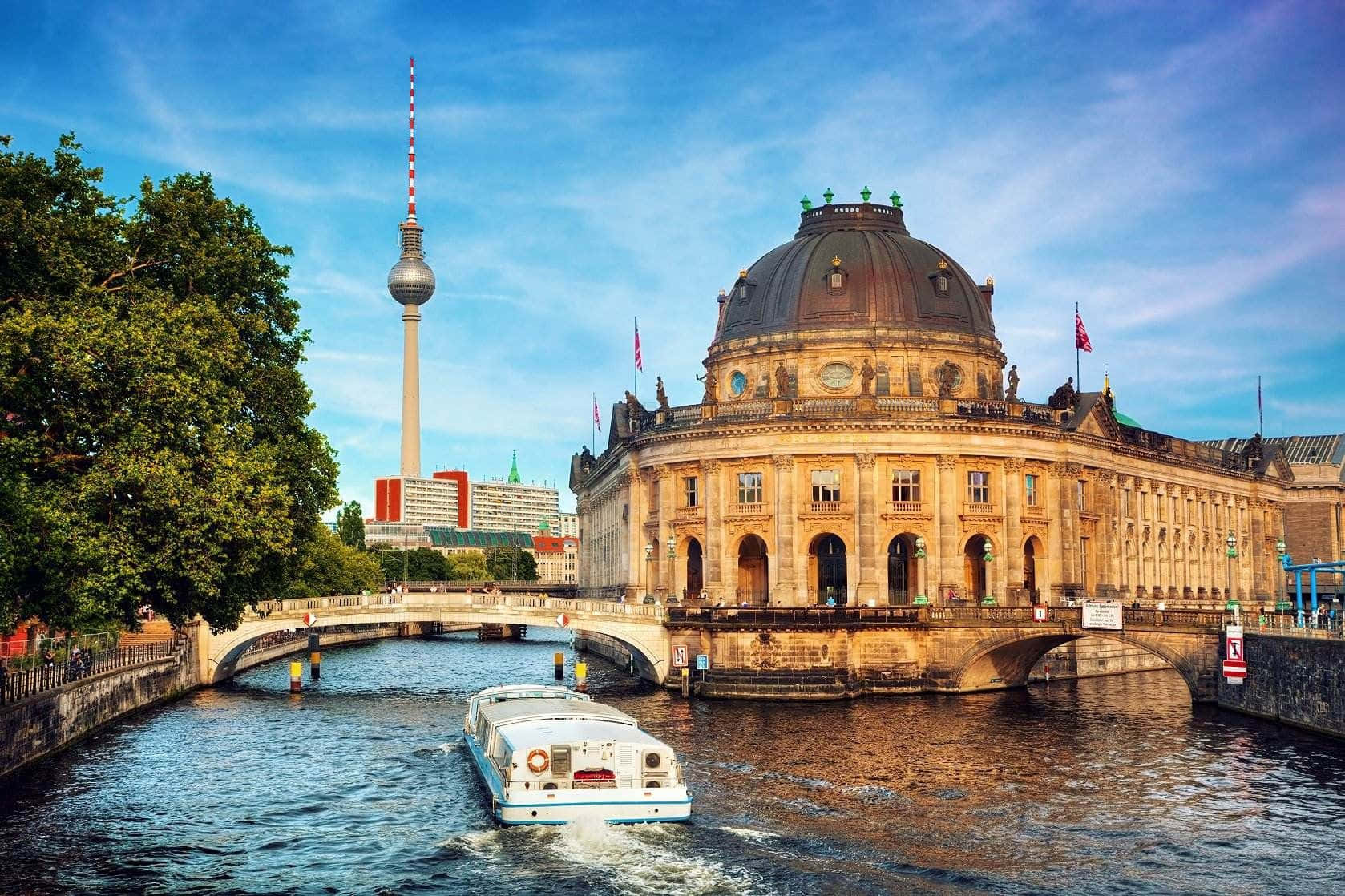 Berlin 桌布 壁紙 — 一艘白色小船在石橋下滑行，旁邊是宏偉的圓頂國會大廈，標誌性的電視塔在明亮的藍天下聳立在背景中。