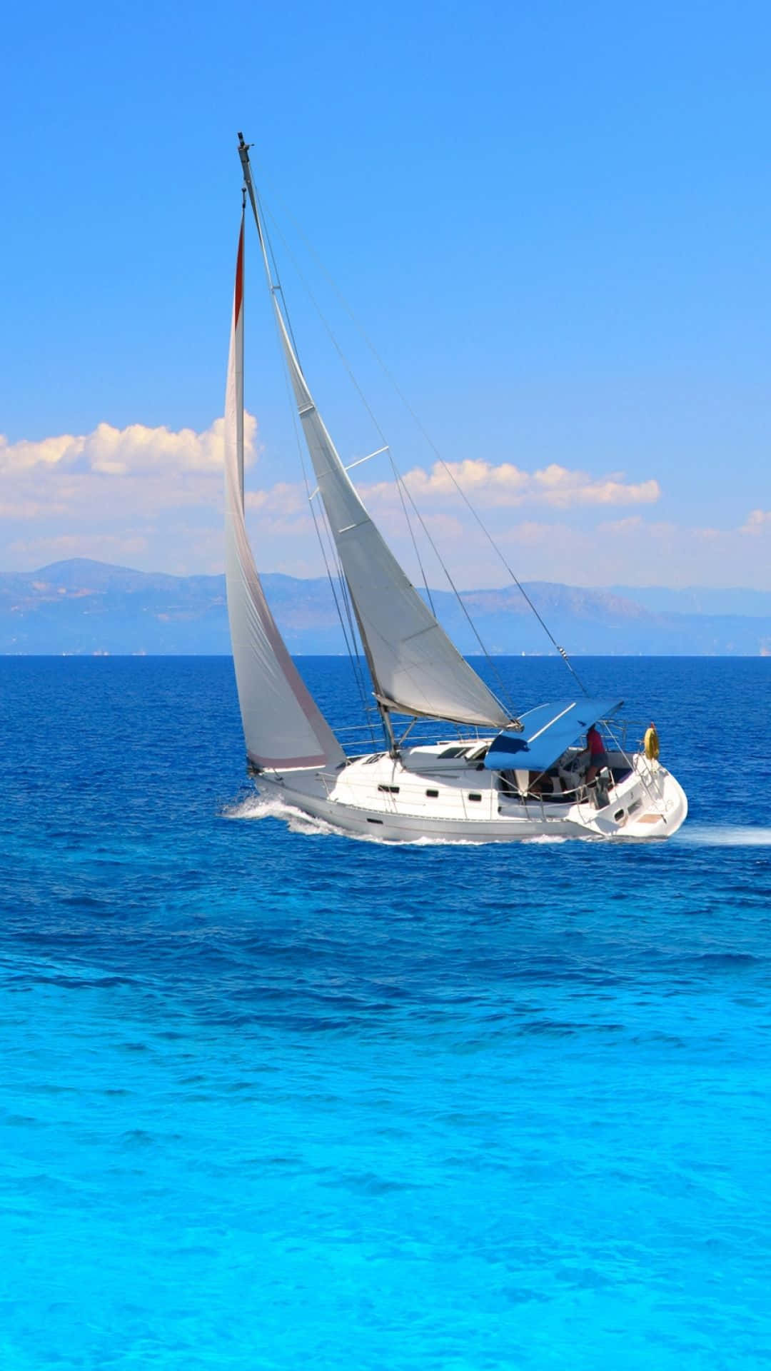 Sailboat 桌布 壁紙 — 一艘白色帆船在清澈藍天下，於充滿活力的碧綠海水中滑行，遠方有山巒。