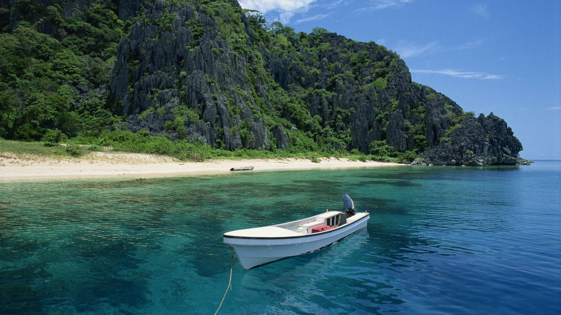 Philippines 桌布 壁紙 — 一艘白色機動船漂浮在清澈碧綠的海水上，旁邊是沙灘，周圍是鬱鬱蔥蔥的綠色懸崖，上方是明亮的藍天。