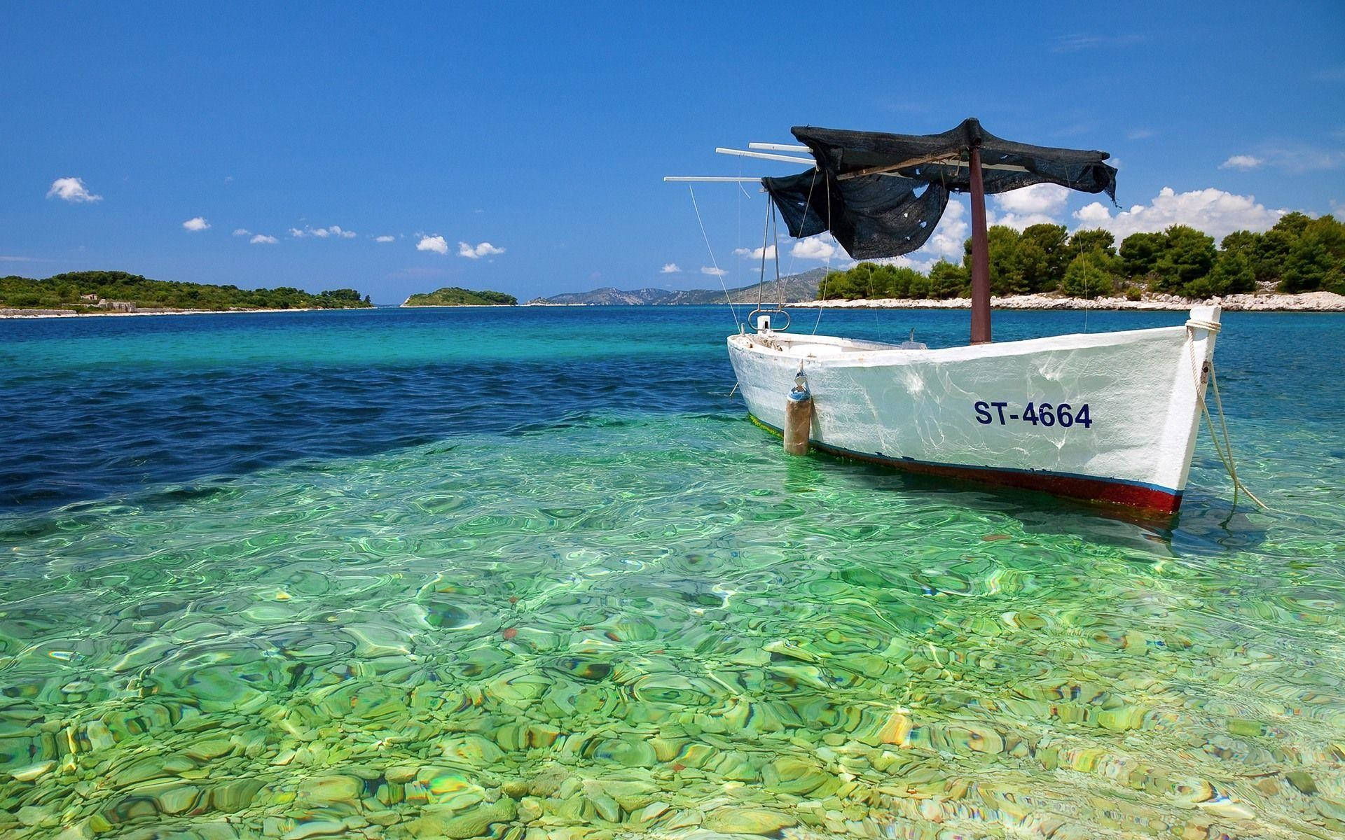 Croatia 桌布 壁紙 — 一艘白色漁船配黑色頂篷，漂浮在清澈碧綠的海水中，靠近綠色島嶼，天空湛藍。