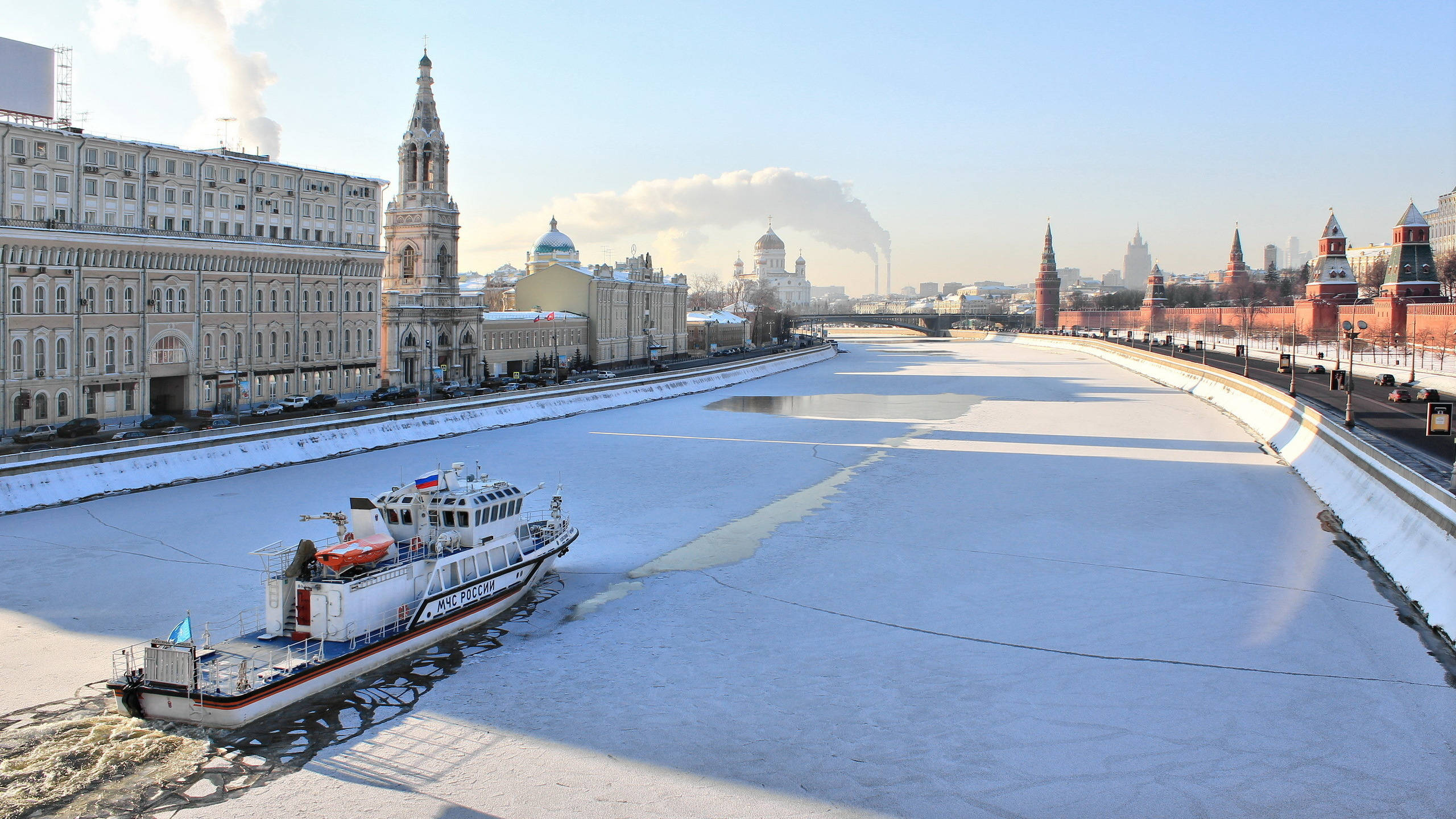 Russia 桌布 壁紙 — 一艘白色破冰船在白雪覆蓋的俄羅斯城市中，穿越結冰的河流，背景有歷史悠久的塔樓和圓頂教堂，天空清澈湛藍。