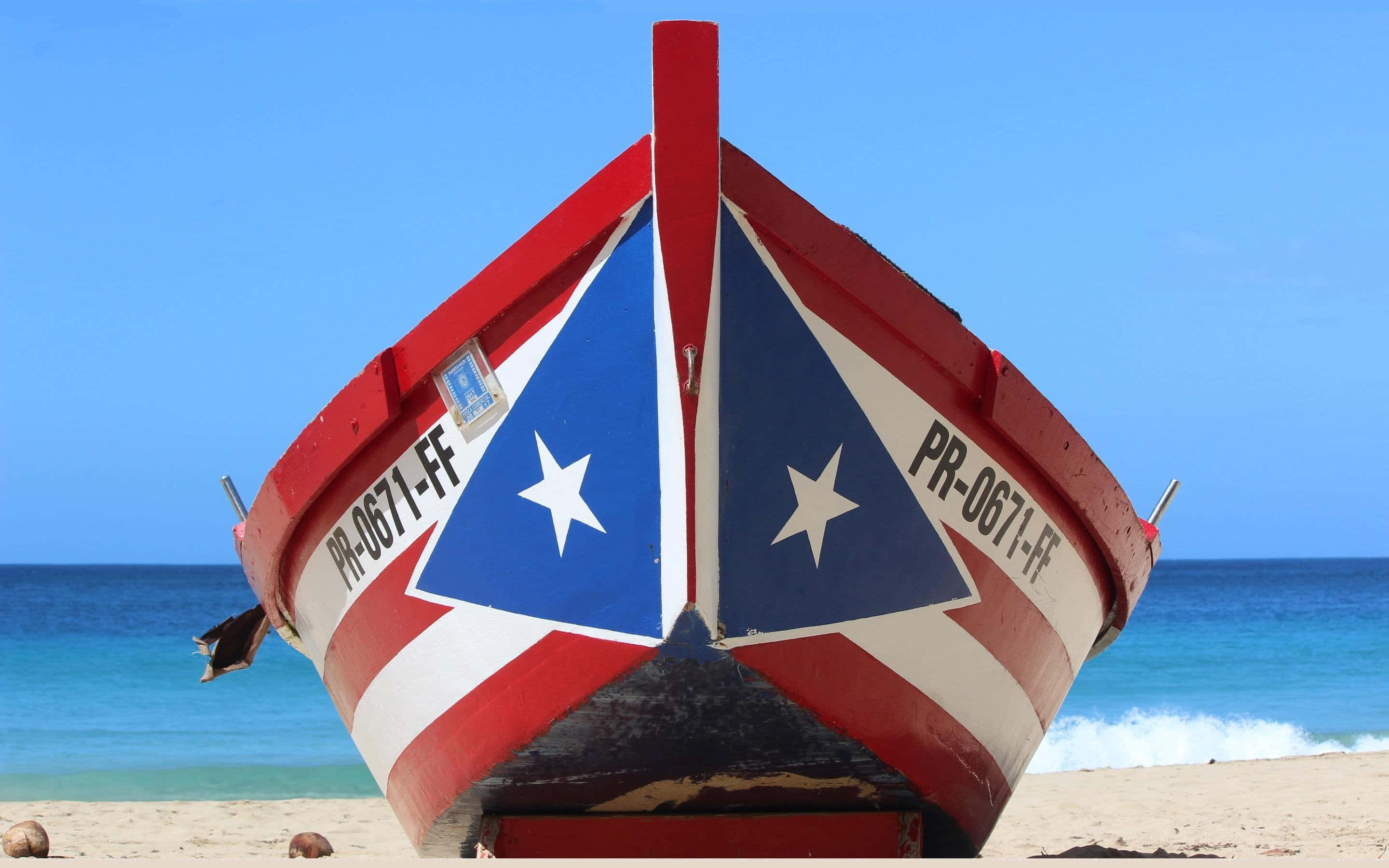 Puerto Rican 桌布 壁紙 — 一艘紅色船上繪有充滿活力的波多黎各旗幟，擱在陽光明媚的沙灘上，伴隨著碧綠的海浪。