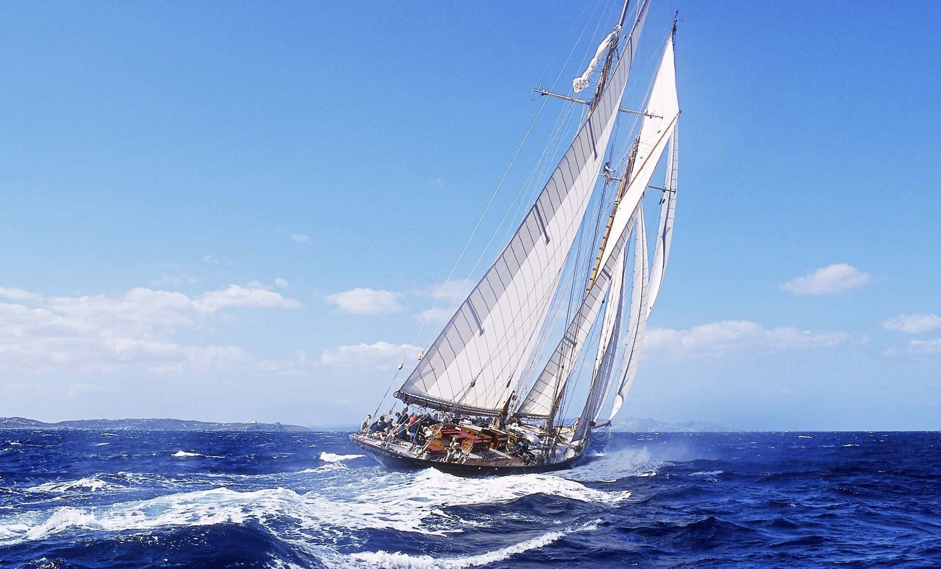 Sailboat 桌布 壁紙 — 一艘經典的高桅帆船，鼓滿白帆，在蔚藍的天空和散落的雲朵下，劃破深藍色的海浪。