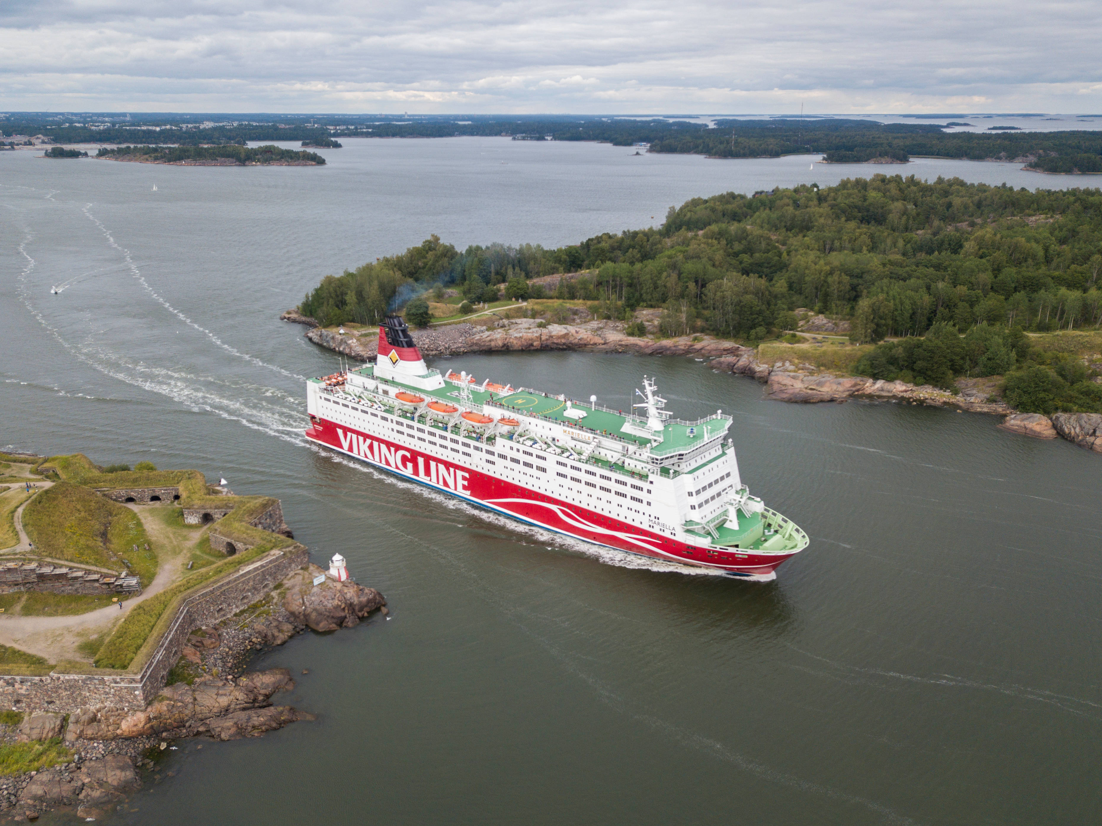 Finland 桌布 壁紙 — 一艘維京航線渡輪在陰天之下，穿過兩旁有森林覆蓋島嶼和岩石海岸的狹窄水道。