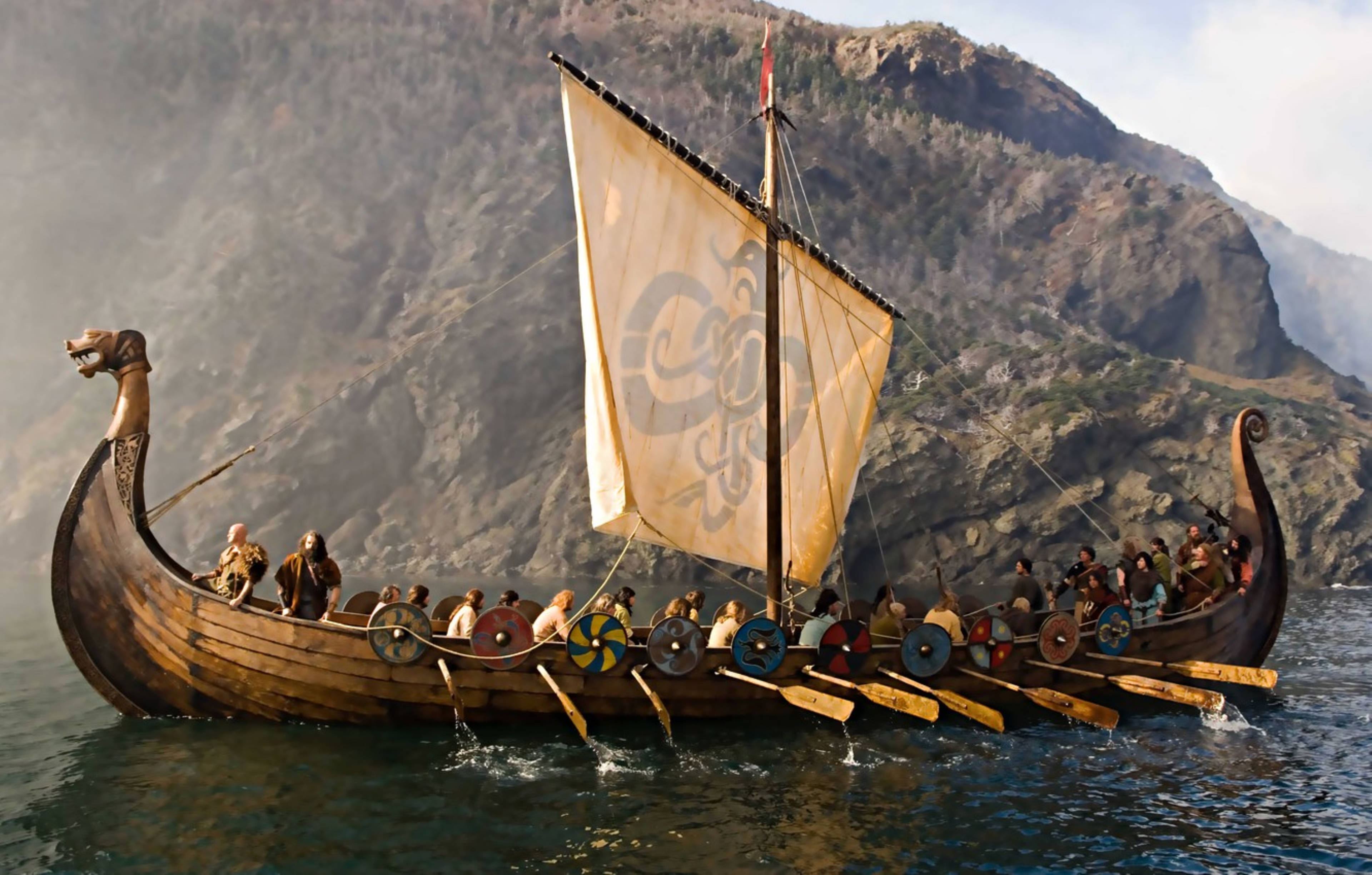 Viking Ship 桌布 壁紙 — 一艘維京長船，船首有龍頭，在朦朧的天空下駛過崎嶇的懸崖。