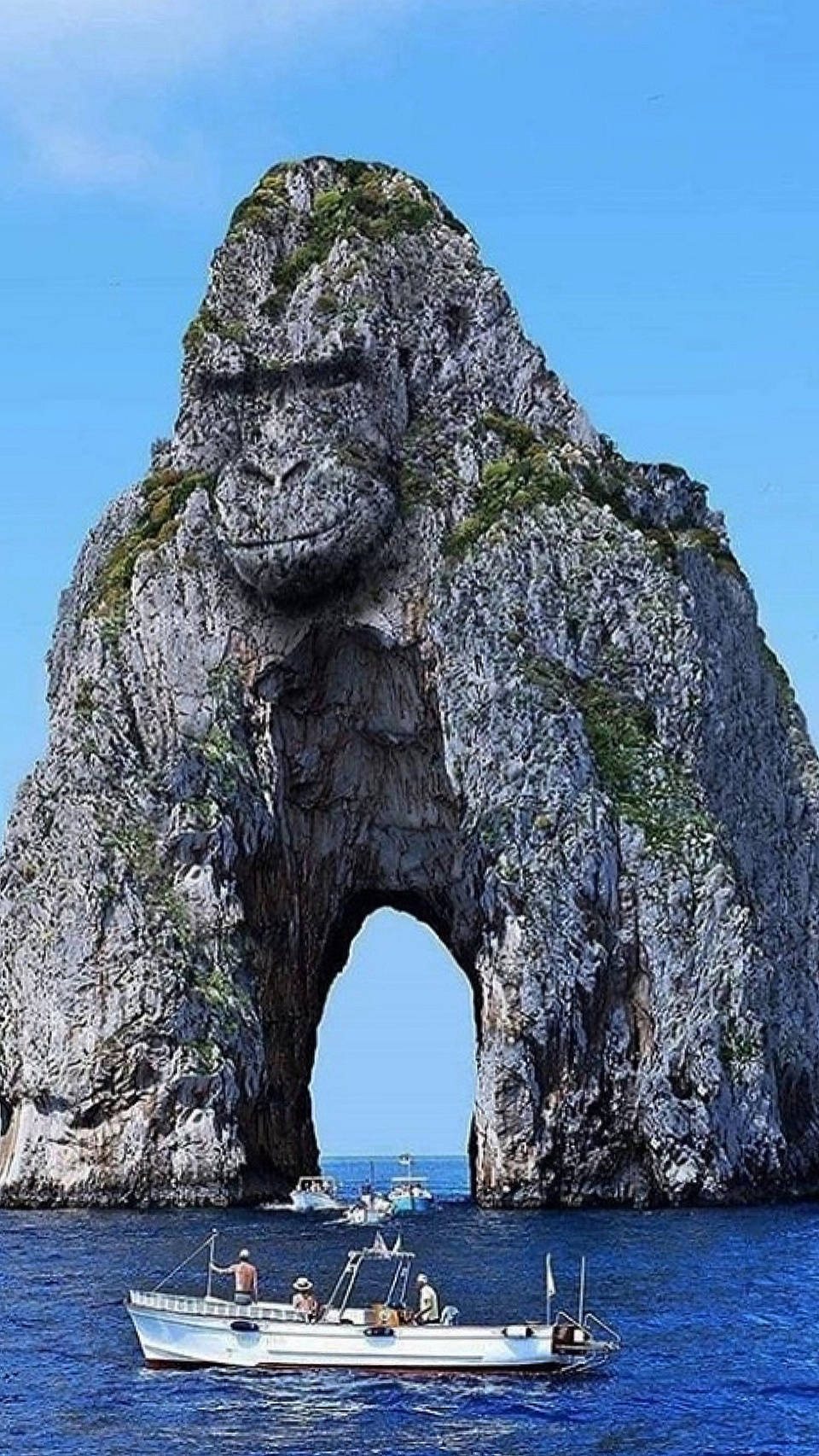 Rock 桌布 壁紙 — 一艘船在義大利卡布里島標誌性的巨型大猩猩形岩石下航行，天空湛藍。