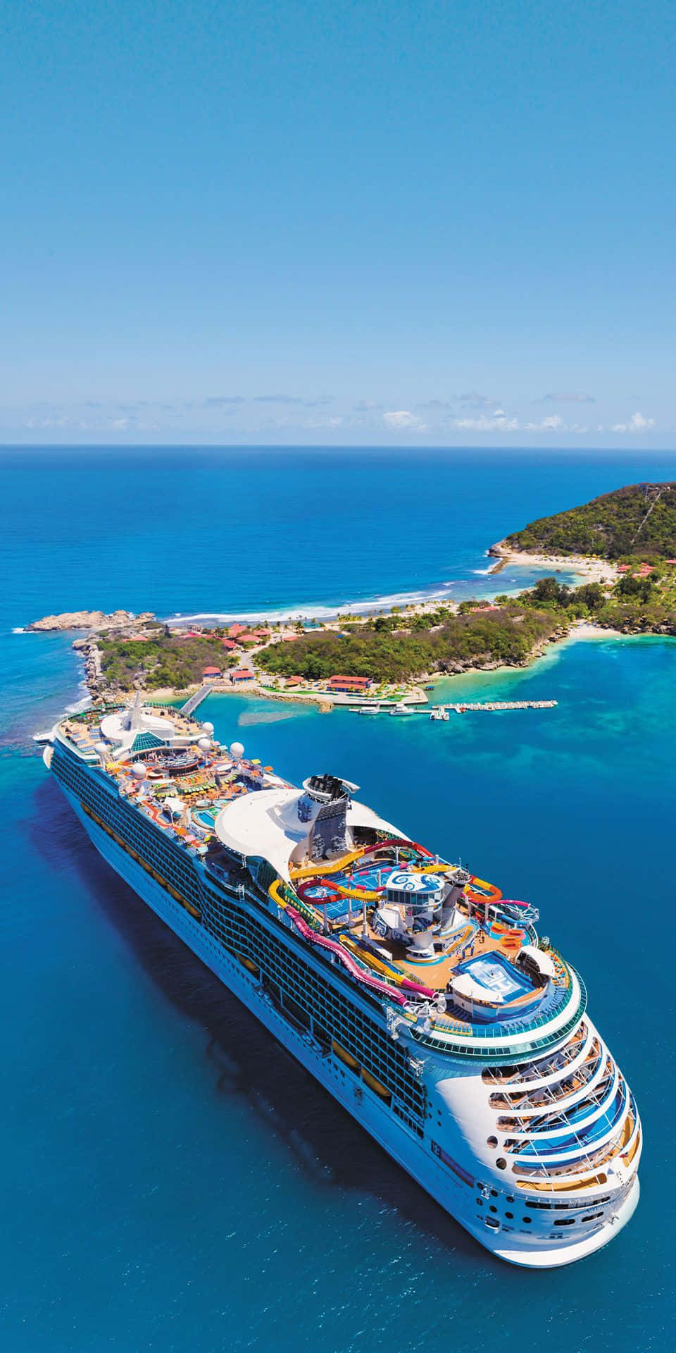 Cruise 桌布 壁紙 — 一艘設有色彩繽紛水上滑梯的巨型郵輪，在鬱鬱蔥蔥的熱帶島嶼附近，滑行於碧綠的海水中。