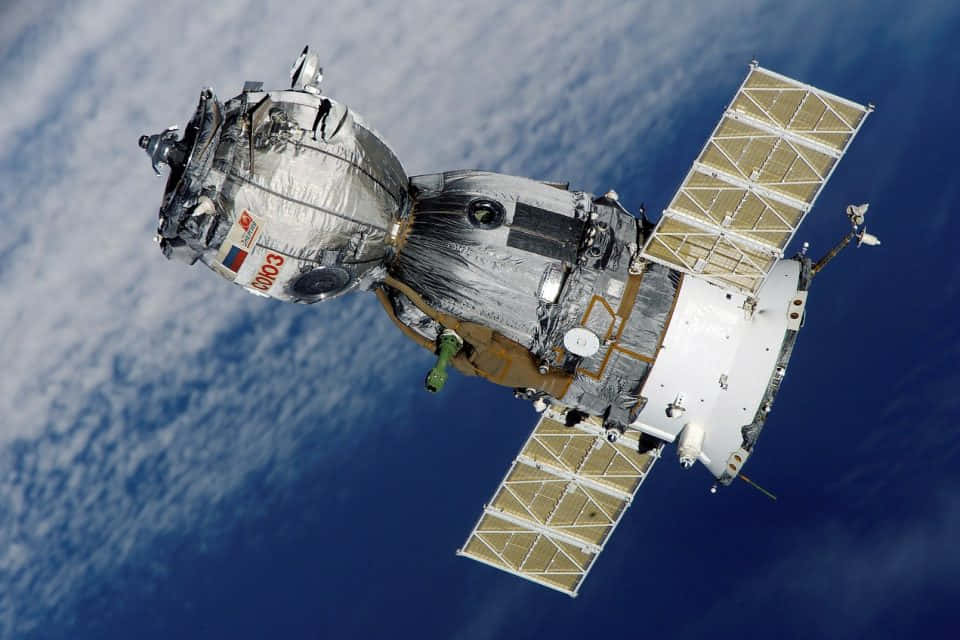 Space Satellite 桌布 壁紙 — 一艘詳細的俄羅斯太空船帶有太陽能電池板，在藍色海洋和白色雲層的背景下繞地球運行。