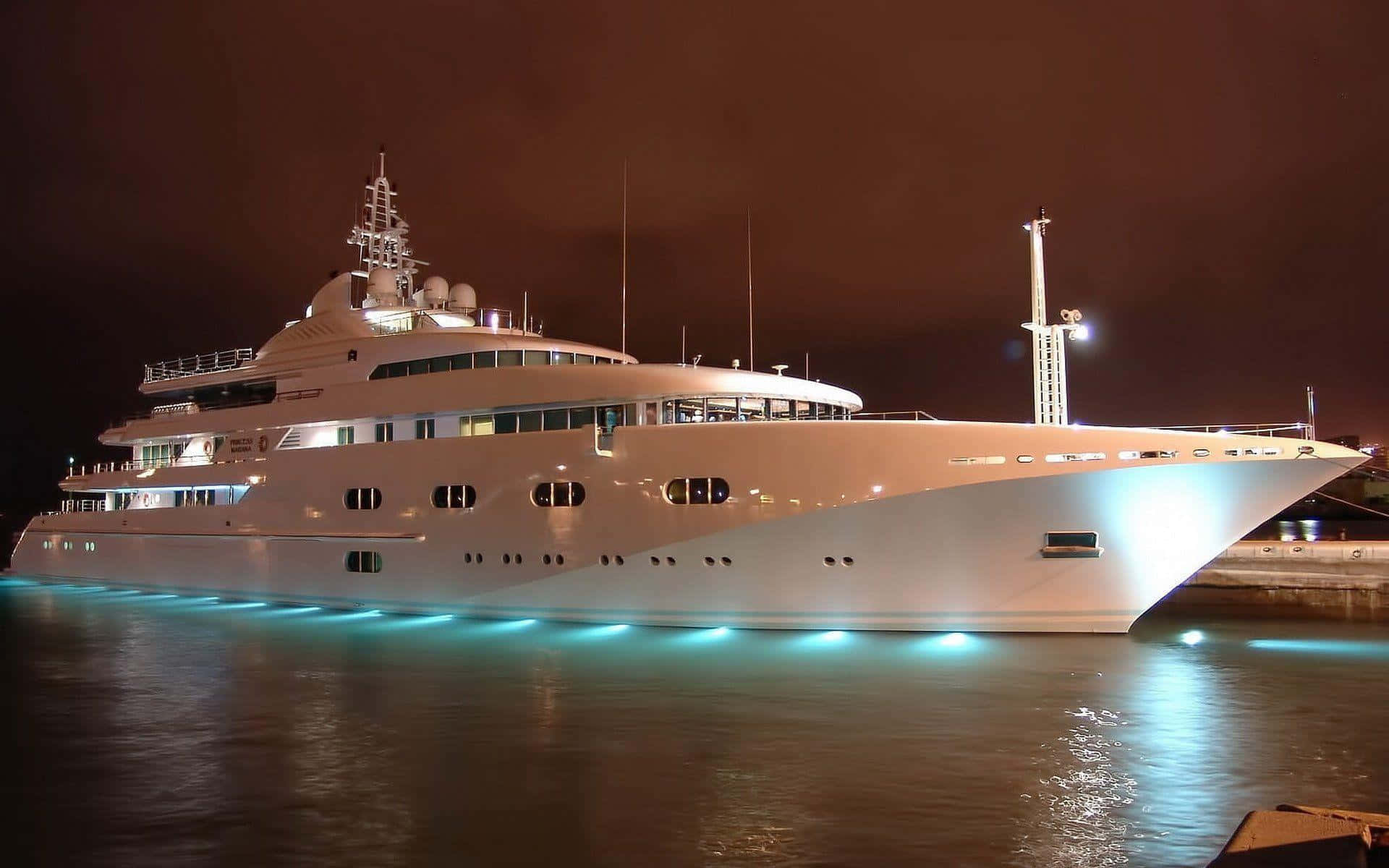 Yacht 桌布 壁紙 — 一艘豪華白色遊艇在夜間發出藍色水下燈光，停泊在黑暗天空下的平靜水域中。