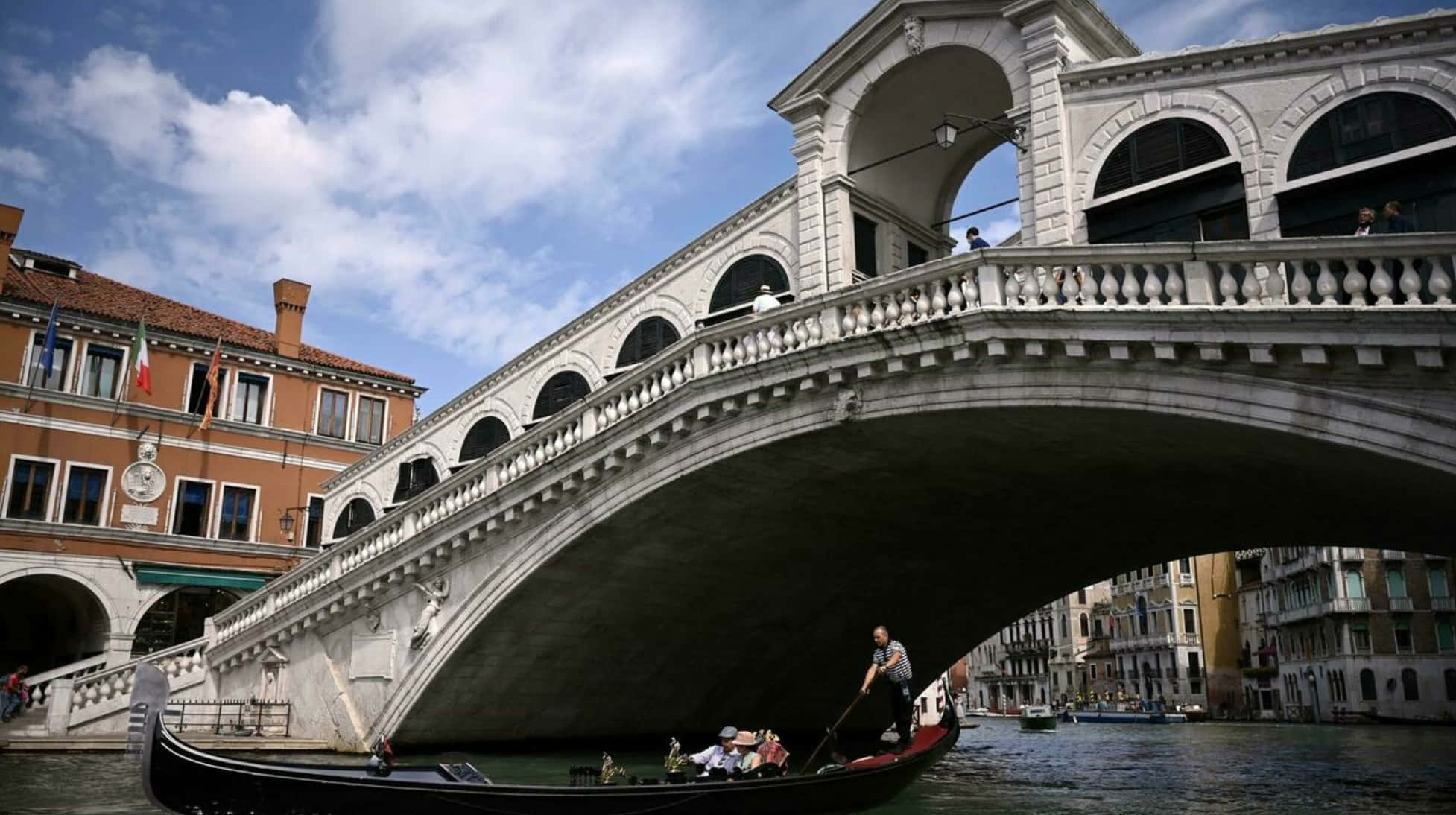 venice 桌布 壁紙 — 一艘貢多拉在威尼斯標誌性的石橋嘆息橋下滑行，歷史建築沿運河排列。