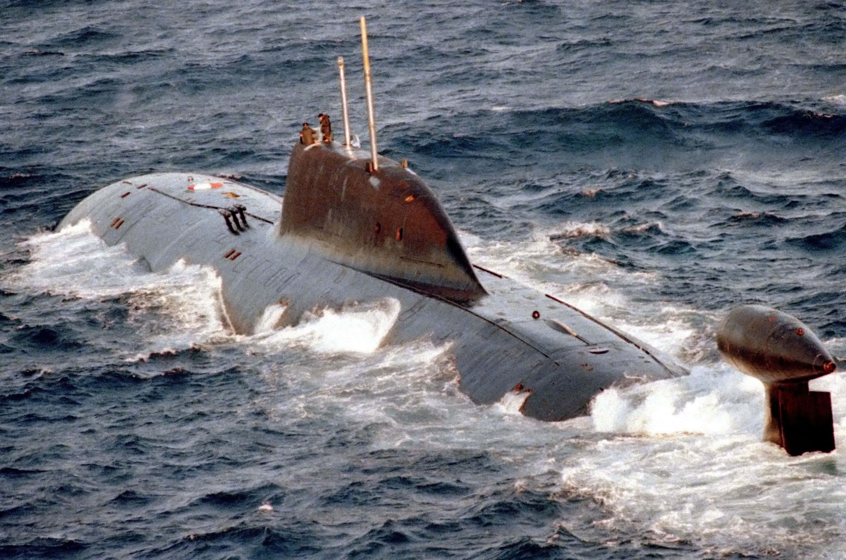 Submarine 桌布 壁紙 — 一艘軍用潛艇在波濤洶湧的藍色海水中浮出水面，指揮塔上可見船員。