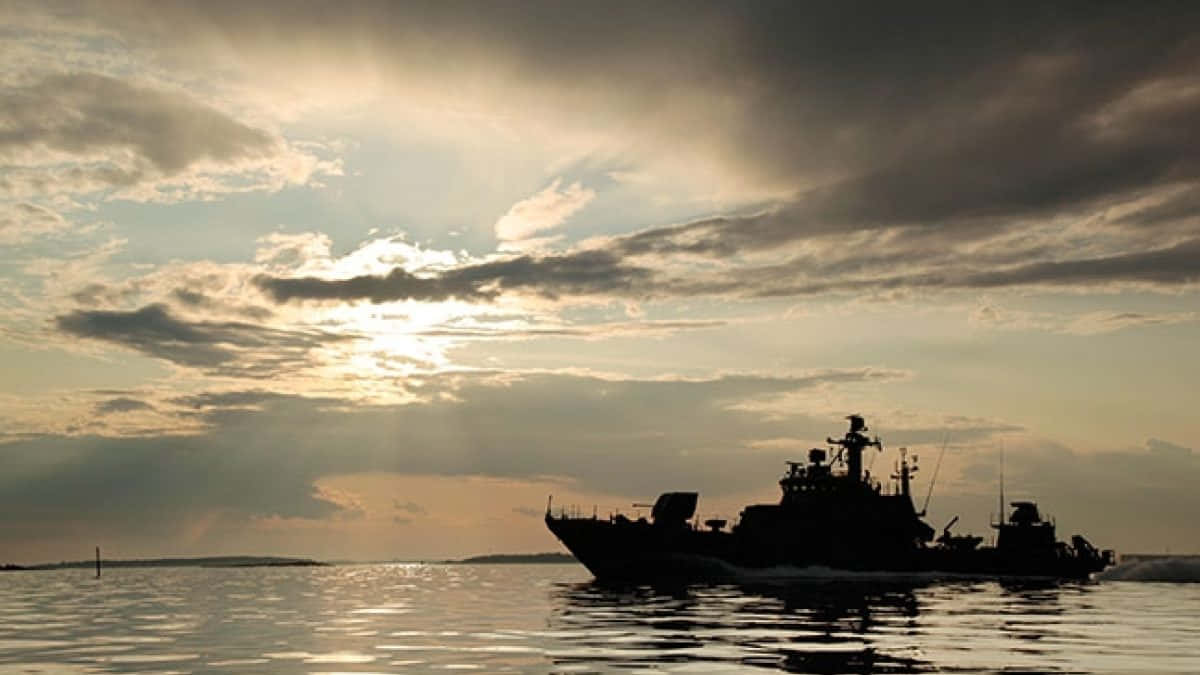 船 桌布 壁紙 — 一艘軍艦在平靜的水面上航行，金色陽光穿過日落時戲劇性的雲層。