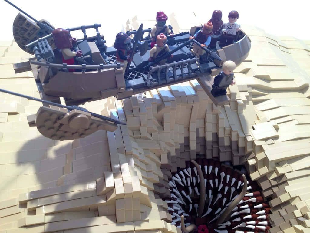 The Sarlacc Pit 桌布 壁紙 — 一艘載有迷你人偶的LEGO星際大戰飛艇懸浮在LEGO建造的峽谷上方，下方有一個尖刺坑。