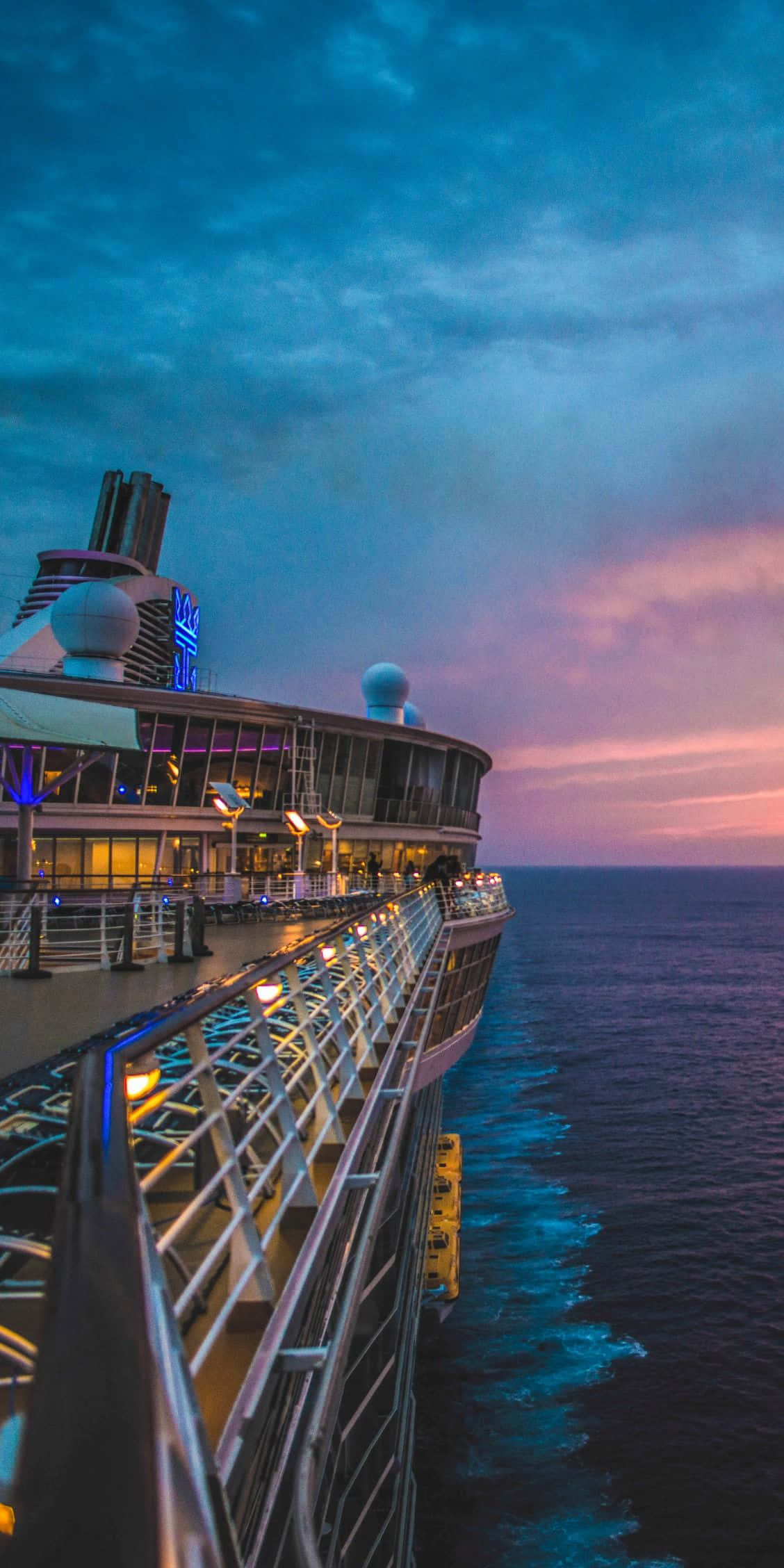 Cruise 桌布 壁紙 — 一艘郵輪的甲板在暮色天空下閃耀著溫暖的燈光，天空被塗成深藍色和柔和的粉紅色，映照在海洋之上。