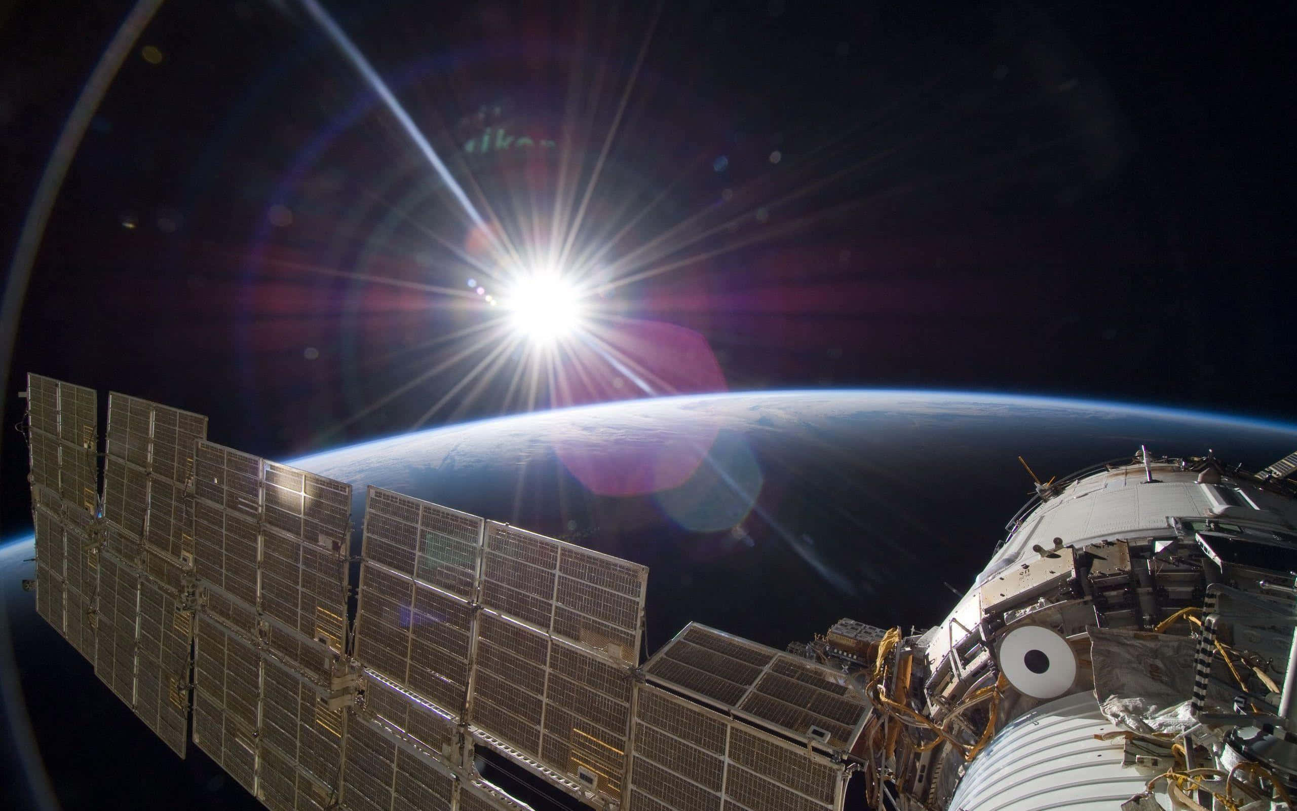Iss 桌布 壁紙 — 一艘配備太陽能板的太空船繞地球運行，太陽在行星彎曲的地平線後方燃燒。