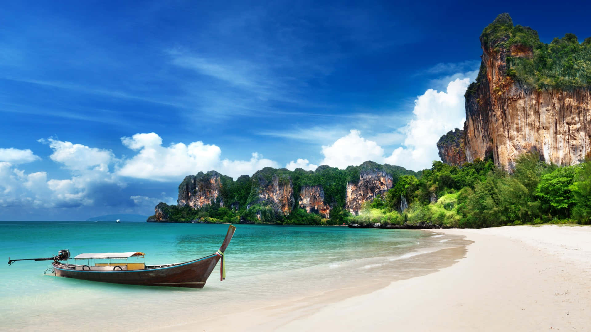 1920x1080 HD Beach 桌布 壁紙 — 一艘長尾船停泊在純淨的白色沙灘上，旁邊是碧綠的海水，背後是茂密的綠植，在明亮的藍天下，雄偉的石灰岩懸崖聳立其間。