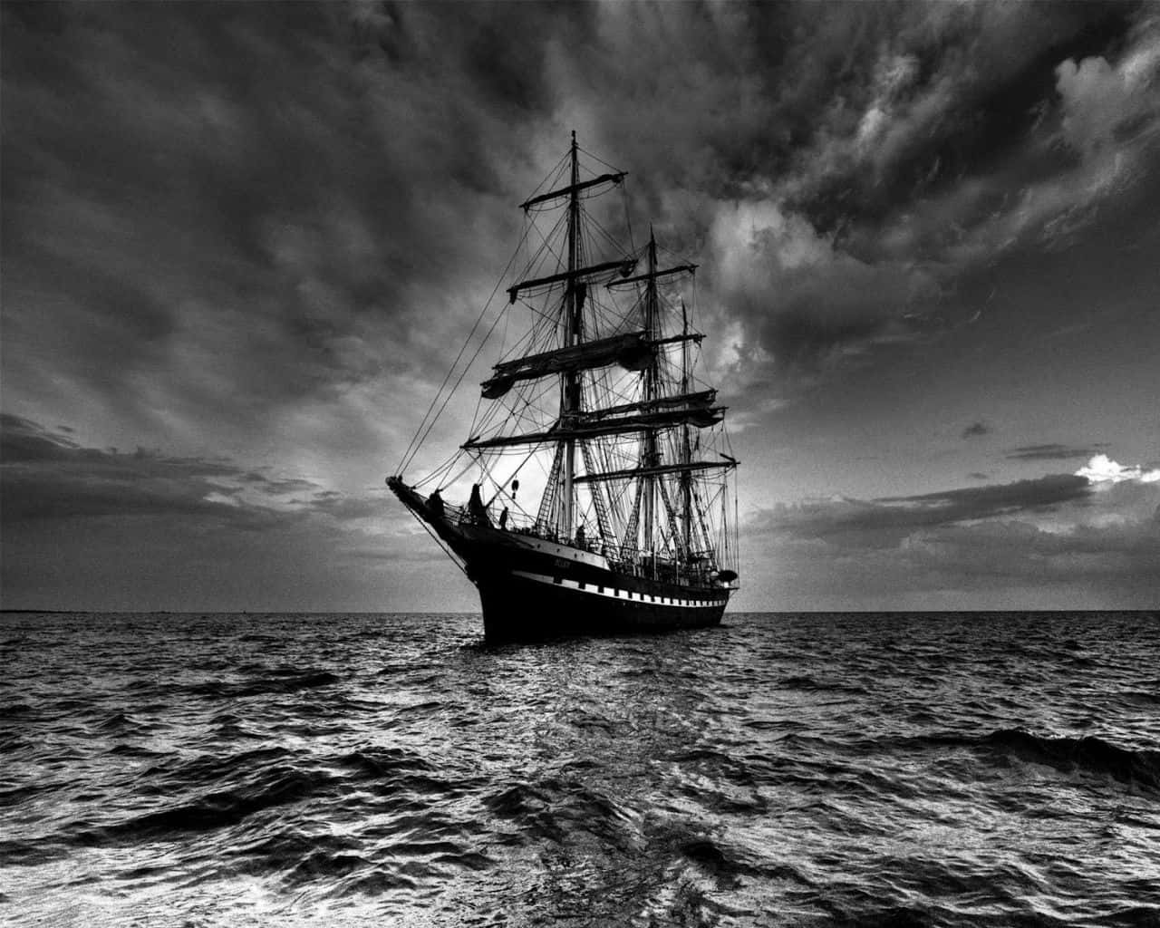 Black And White Storm 桌布 壁紙 — 一艘雄偉的高桅帆船在黃昏時分戲劇性的多雲天空下獨自航行，呈現單色調。